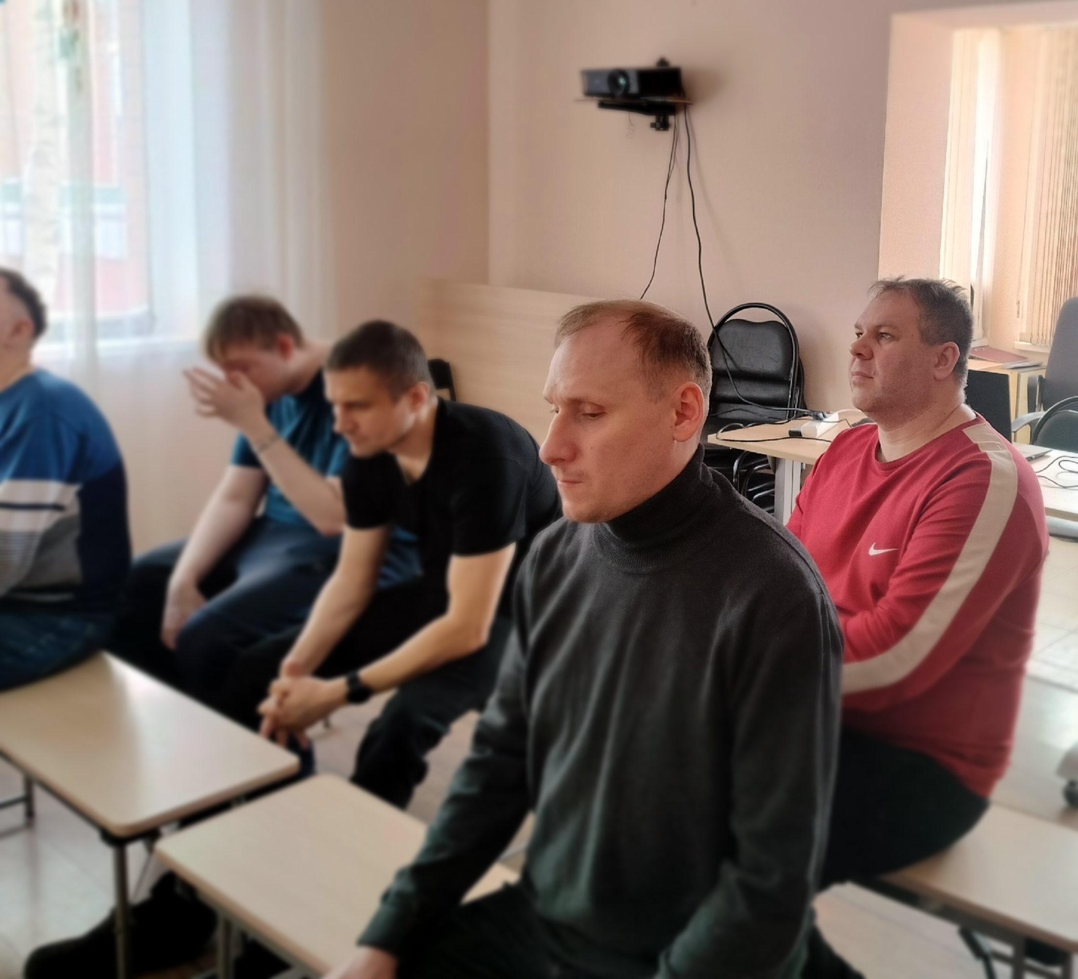 Крупный план нескольких мужчин, сидящих на скамейках и внимательно смотрящих вперед во время показа фильма.