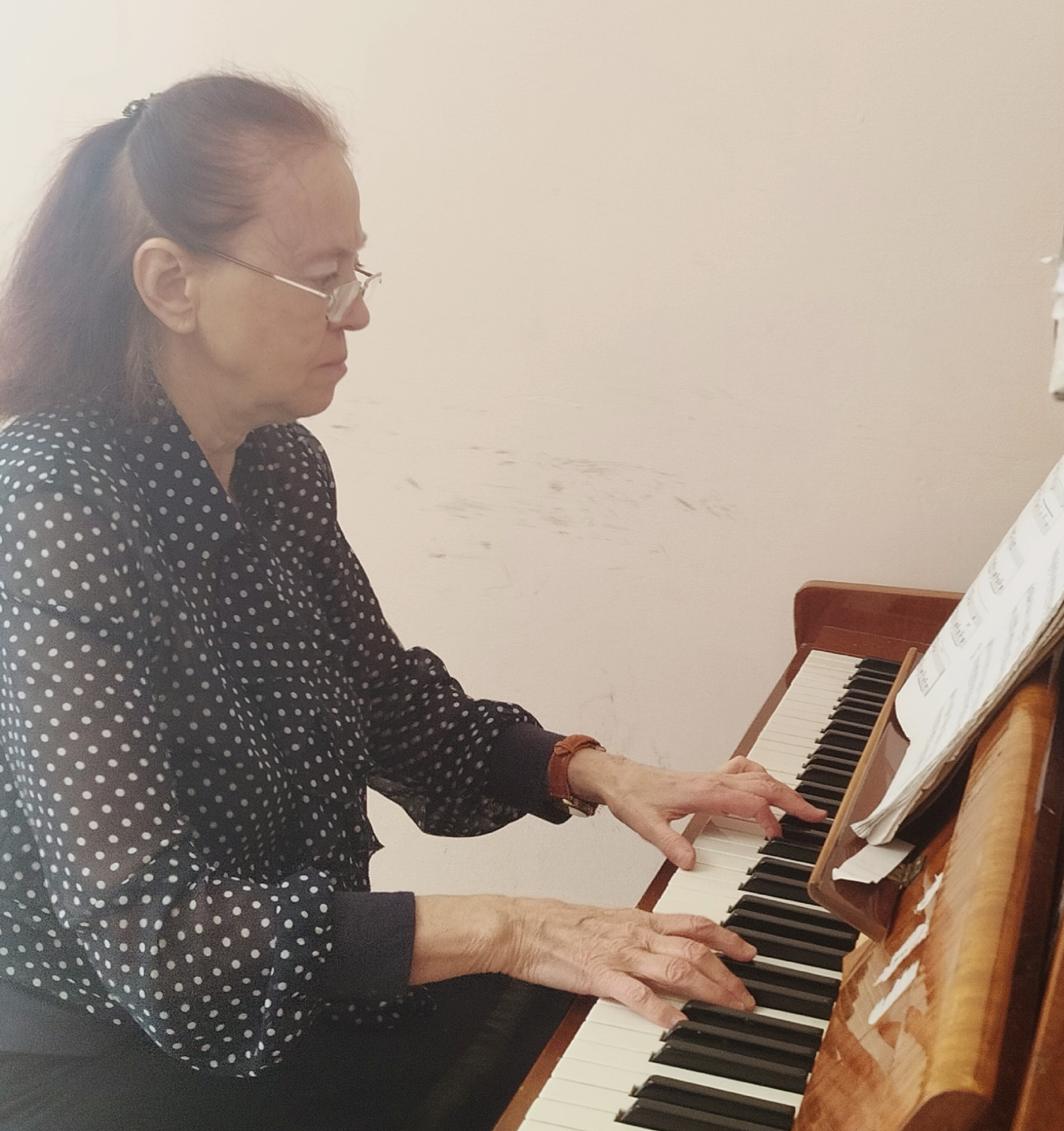 Елена Ароновна Толчинская в очках играет на пианино по нотам.