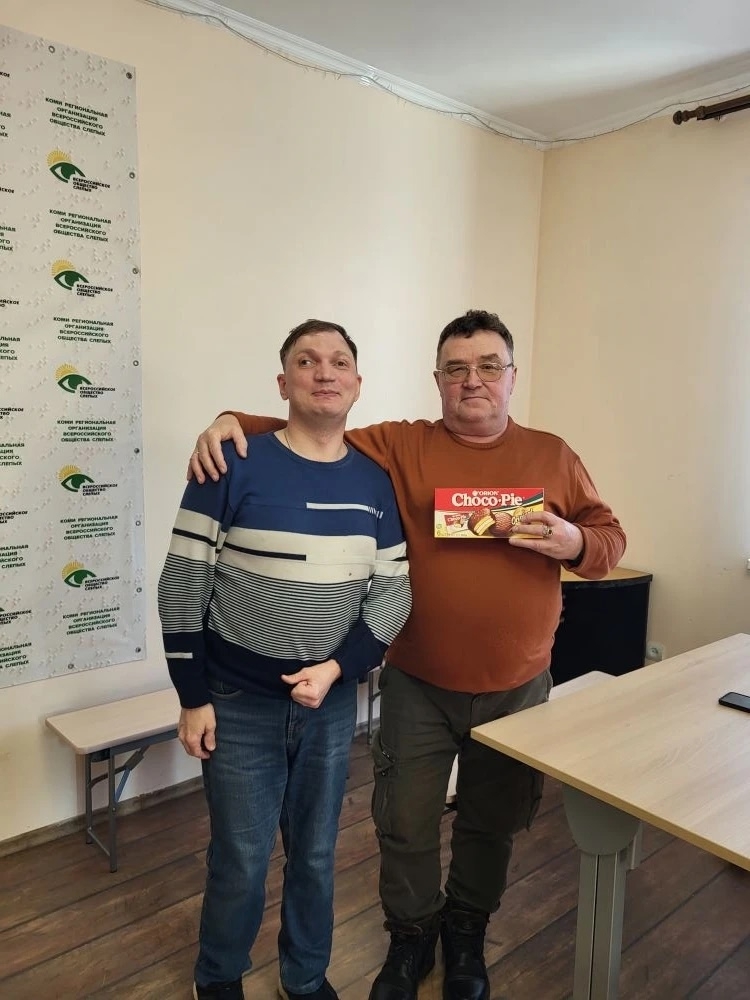 Два мужчины стоят рядом, один держит в руках коробку Choco-Pie, на фоне баннер "Всероссийское общество слепых".