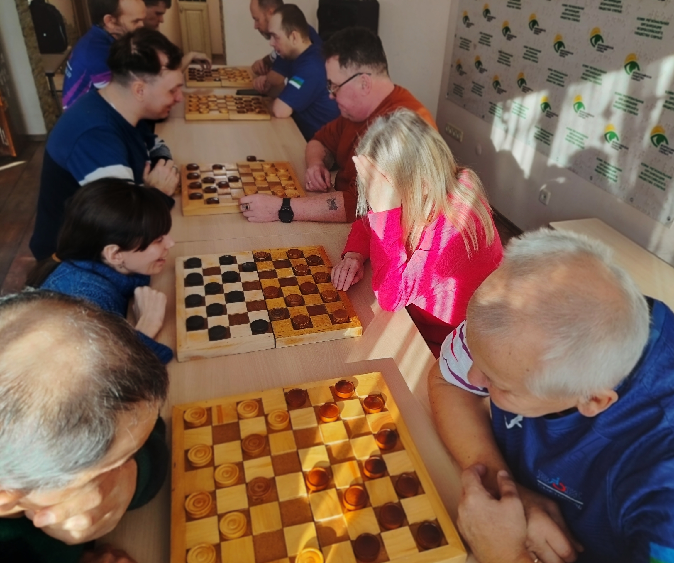 Вид сверху на несколько столов, где участники турнира увлеченно играют в шашки, погруженные в процесс.