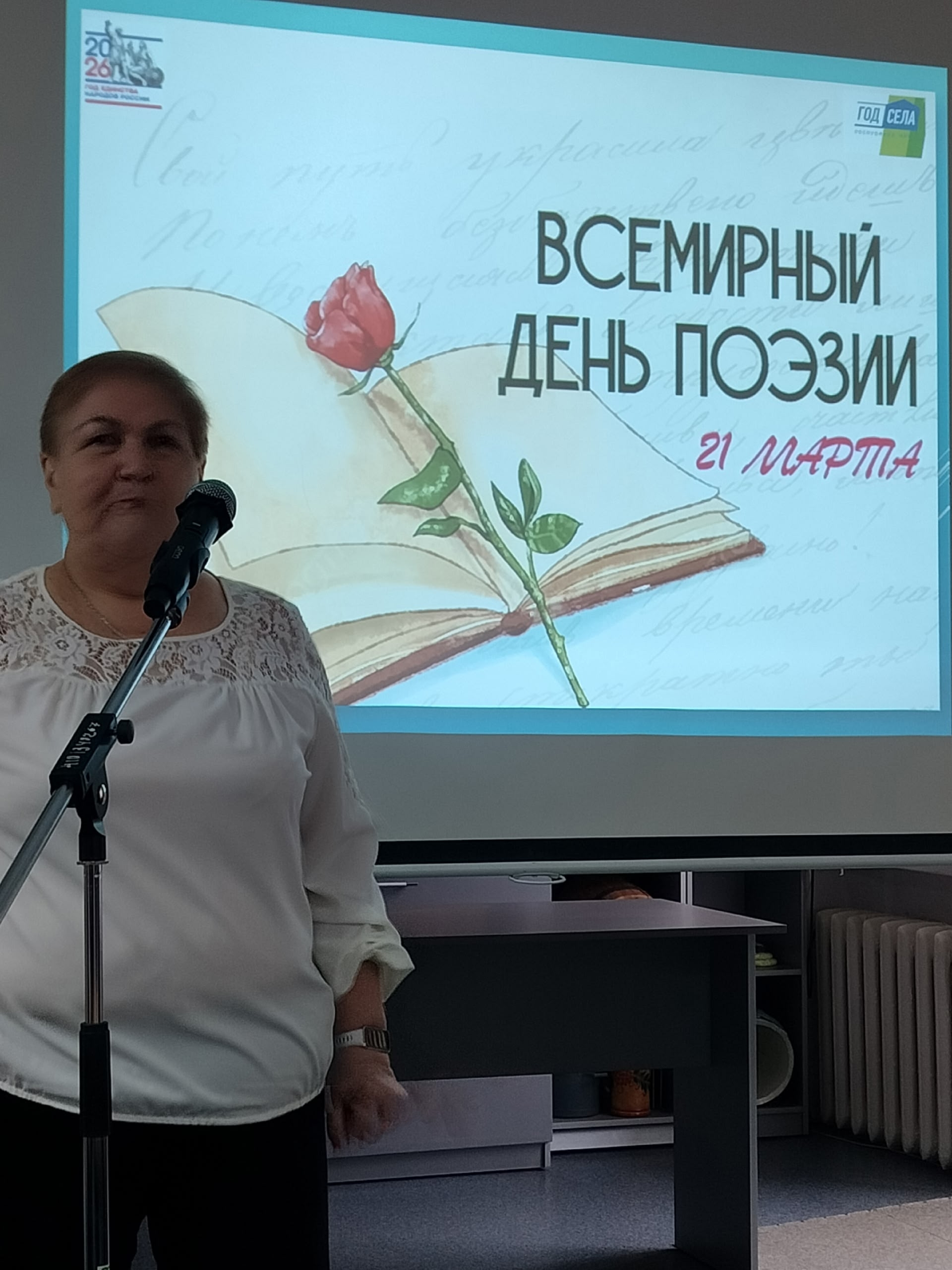 Женщина у микрофона на фоне проекции "Всемирный день поэзии".