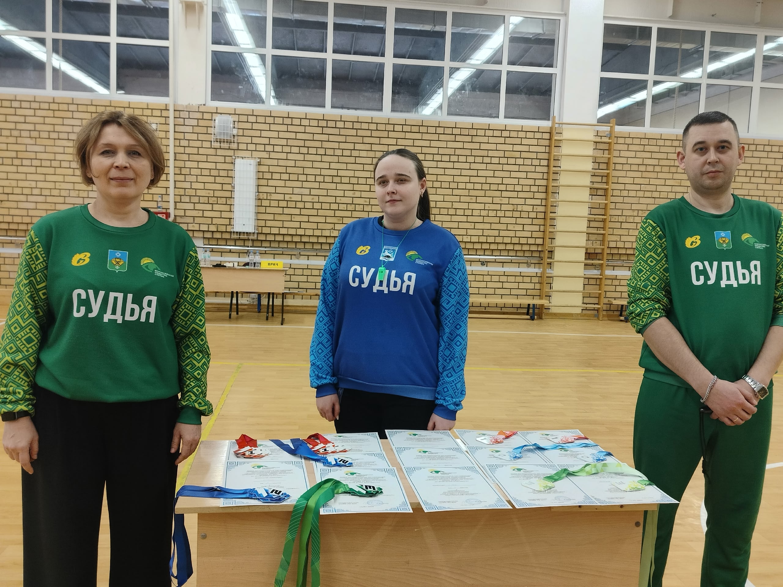 Судьи стоят за столом с наградами в спортзале.