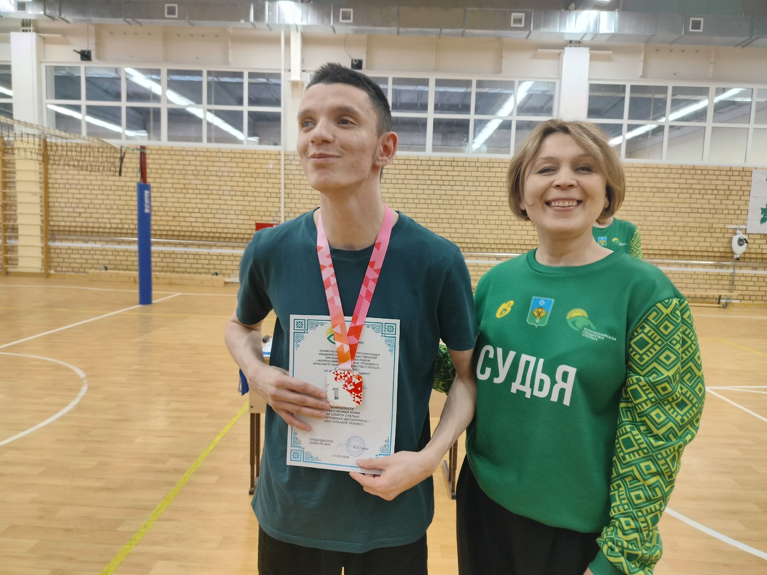 Молодой спортсмен с медалью и сертификатом, рядом судья