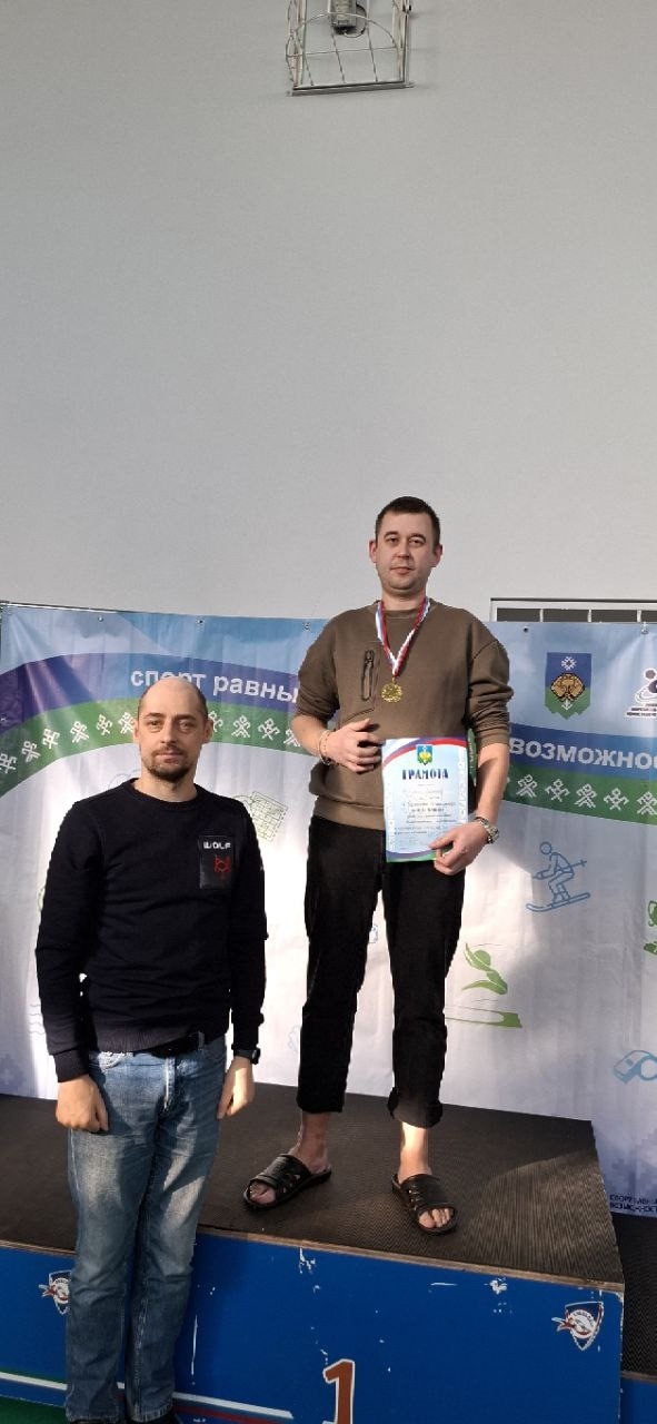 Двое мужчин на пьедестале, один получает медаль и грамоту.