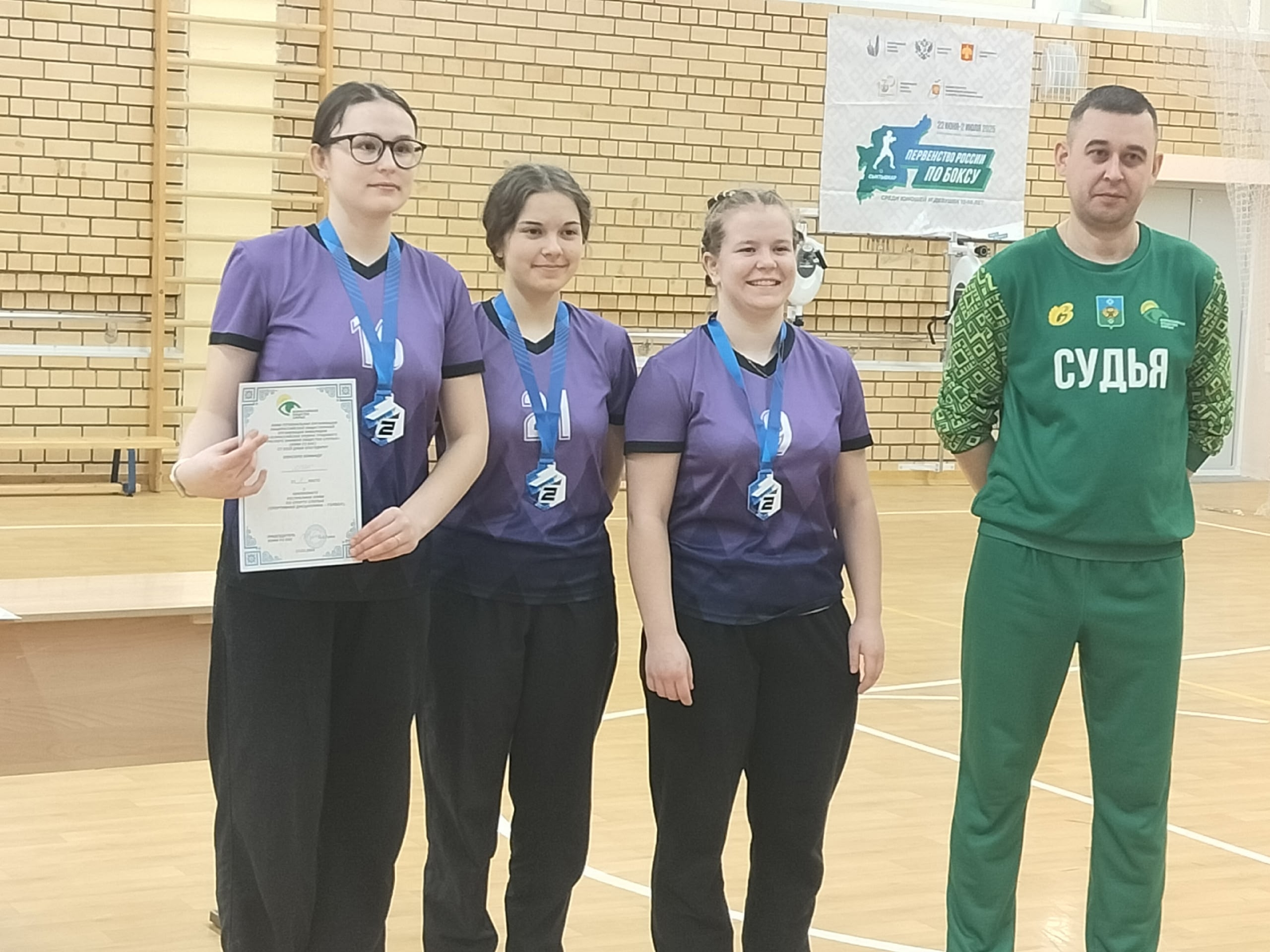 Три девушки с медалями и сертификатом, рядом судья.