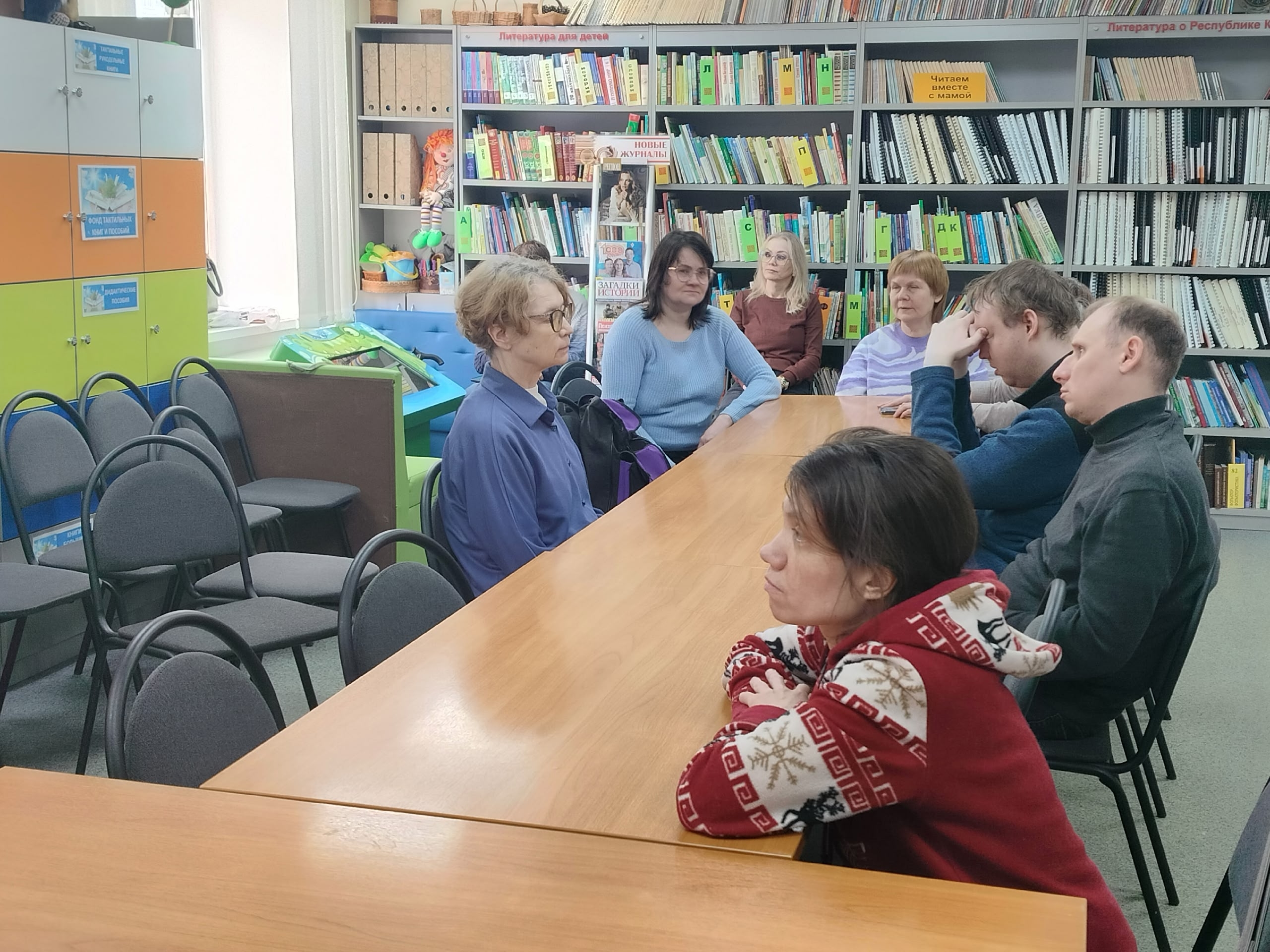 Группа людей за столом в библиотеке с книжными полками