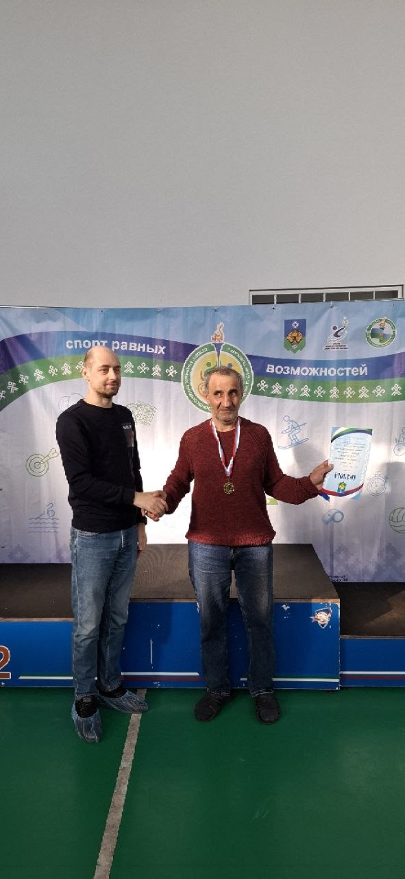 Двое мужчин на пьедестале почета, один вручает другому медаль и грамоту.