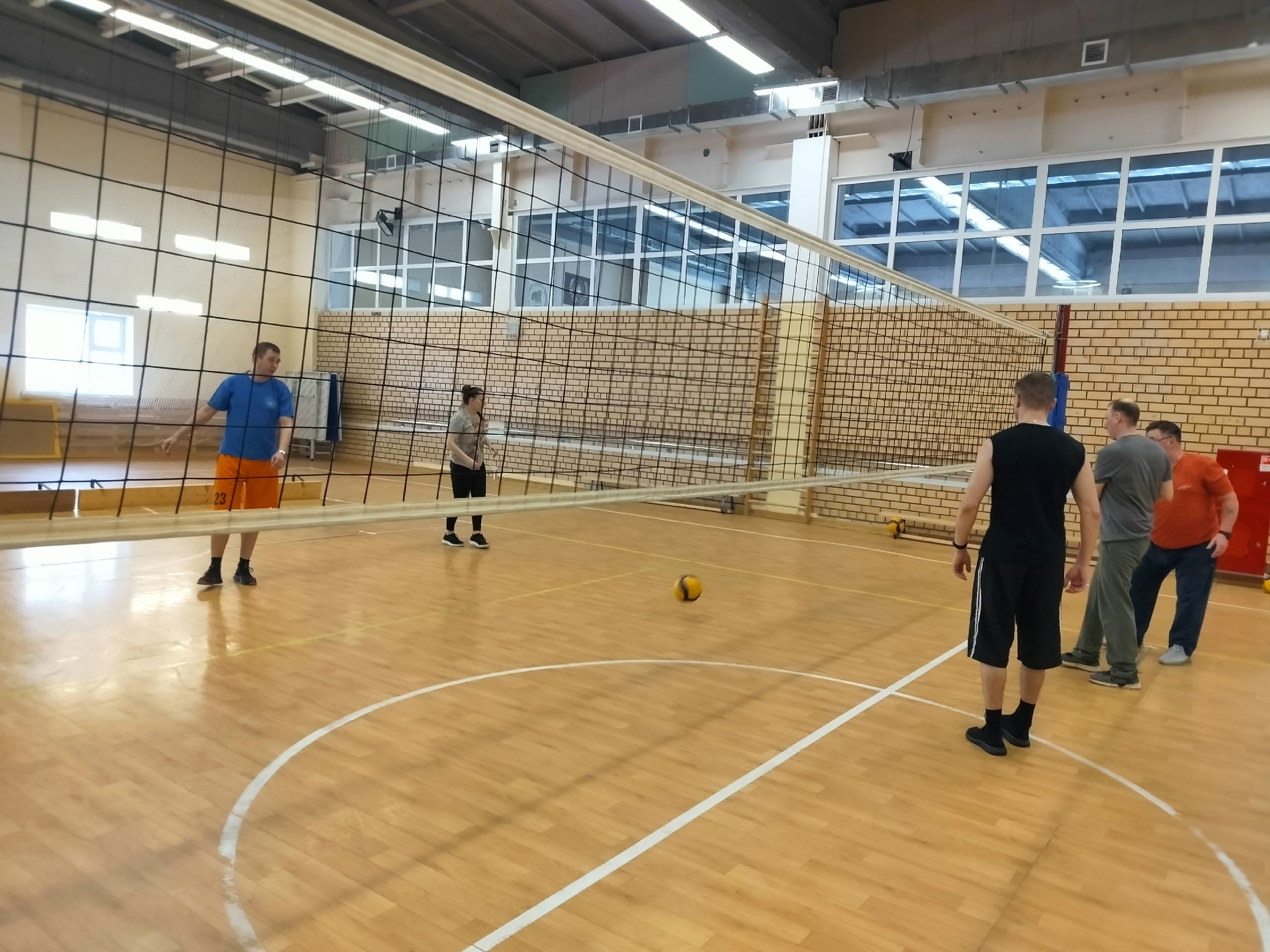 Группа людей на волейбольной площадке с сеткой и мячом на полу.