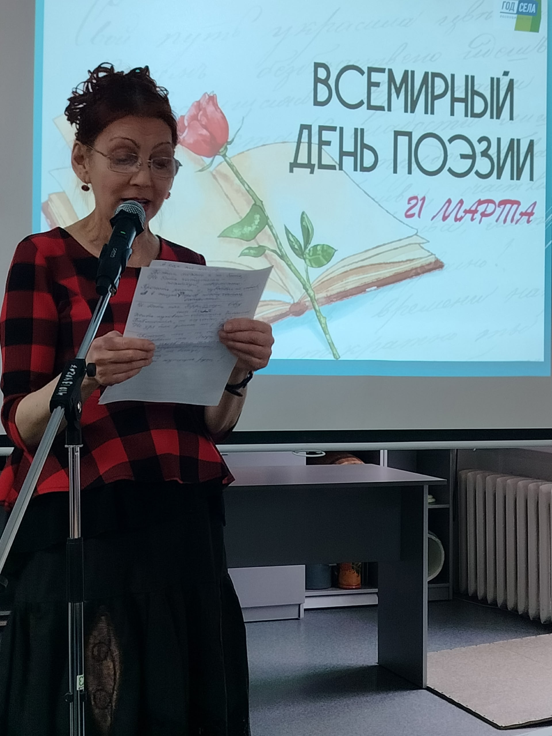 Женщина читает стихи у микрофона на фоне проекции.