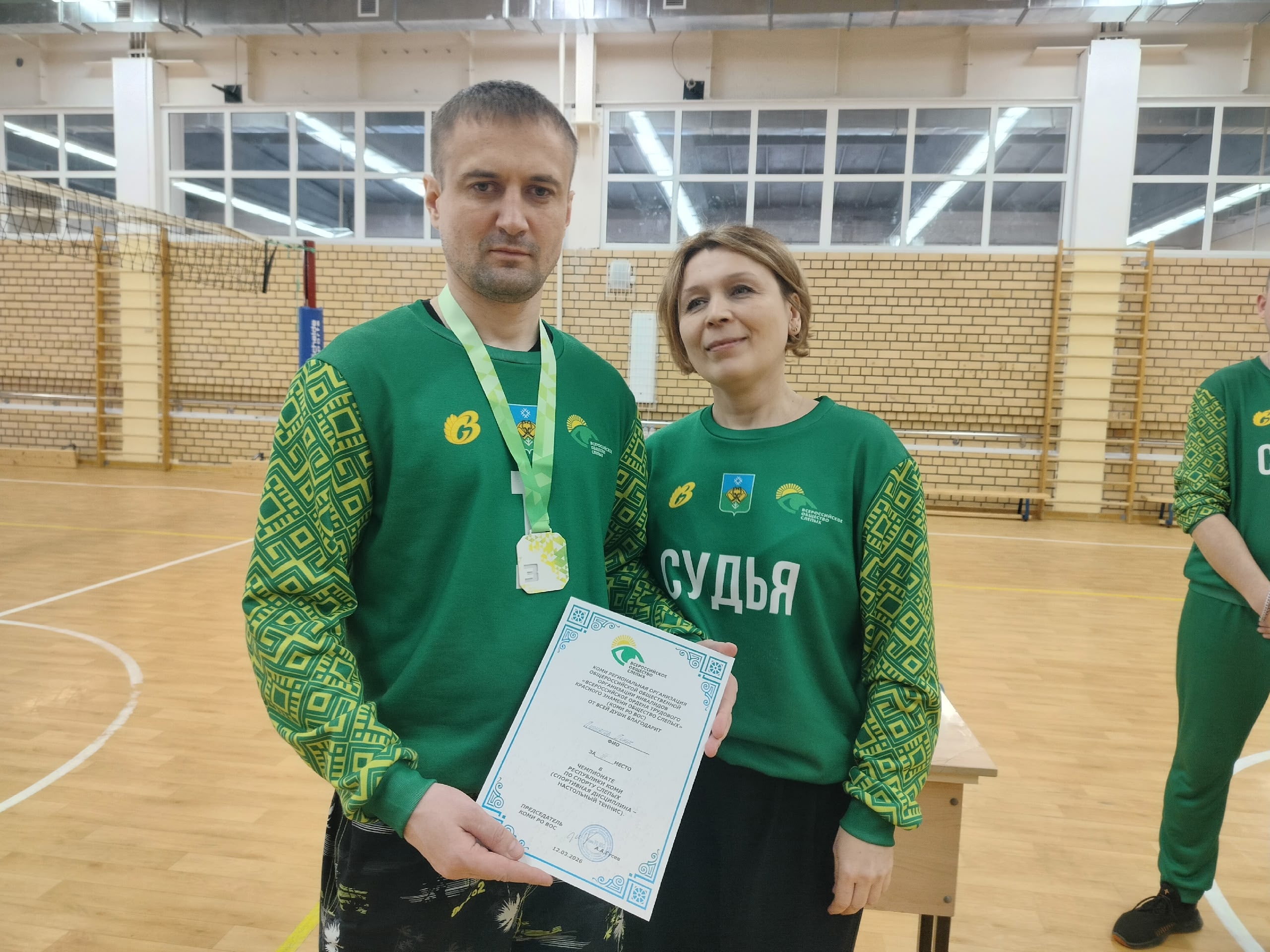 Мужчина с медалью и сертификатом рядом с женщиной-судьей
