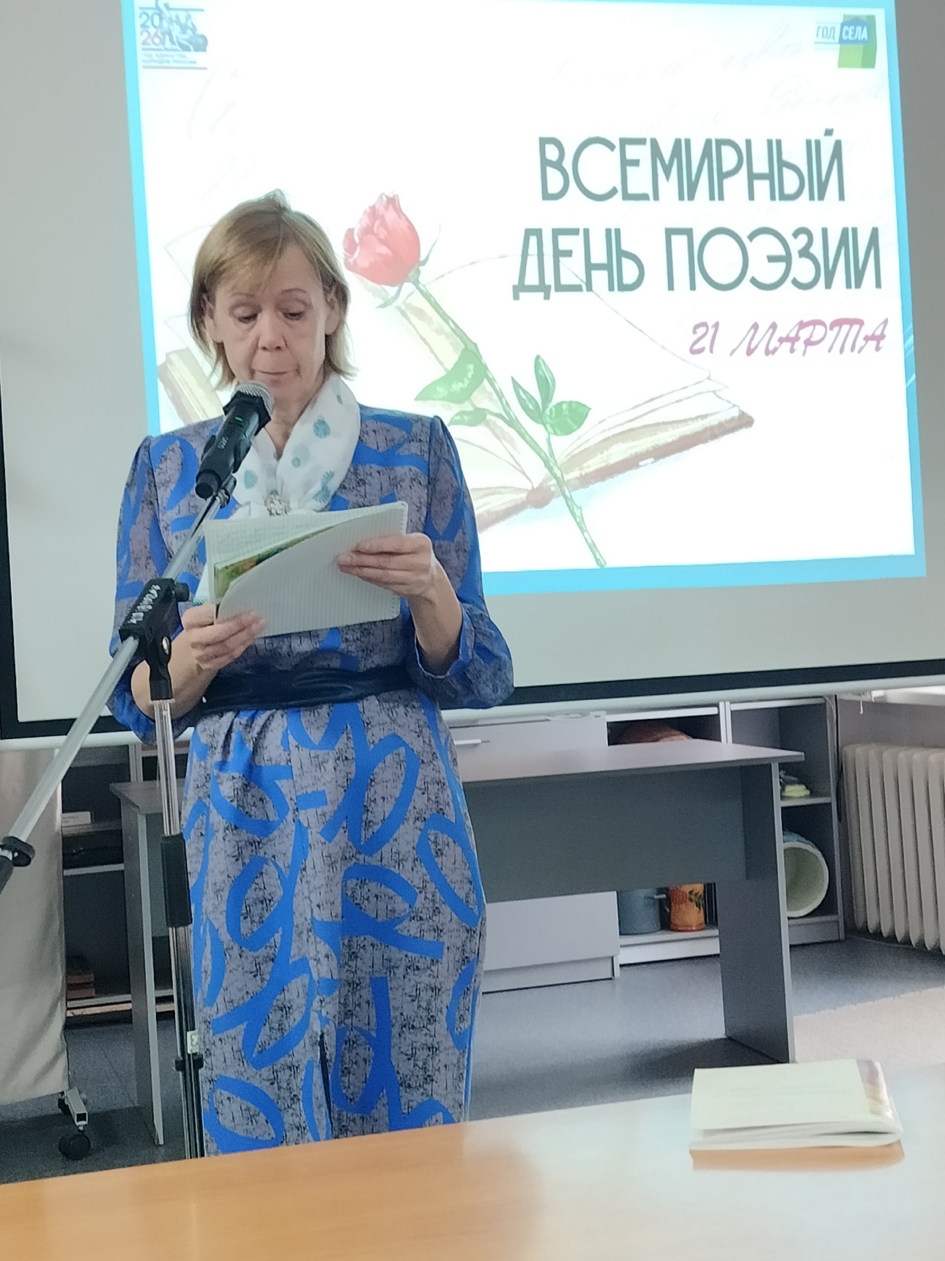 Женщина выступает у микрофона на фоне экрана с надписью.
