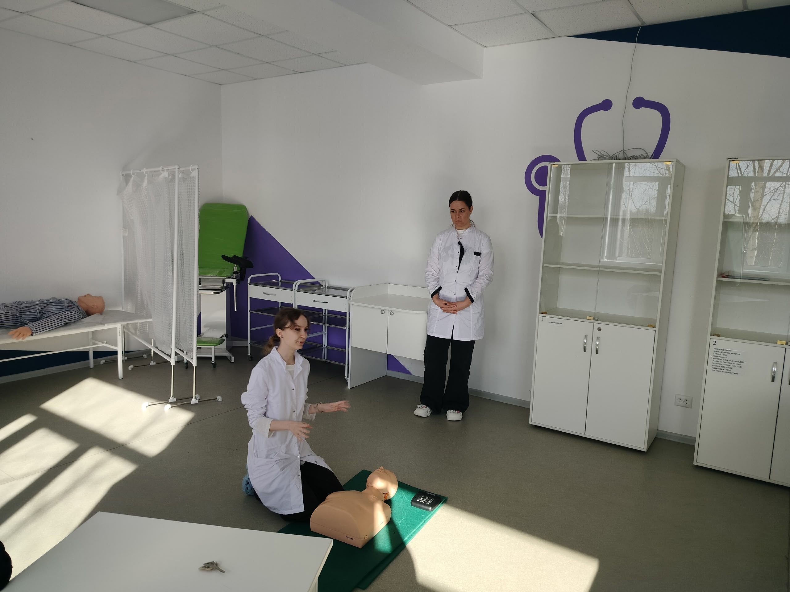 Две женщины в медицинских халатах в учебной комнате.