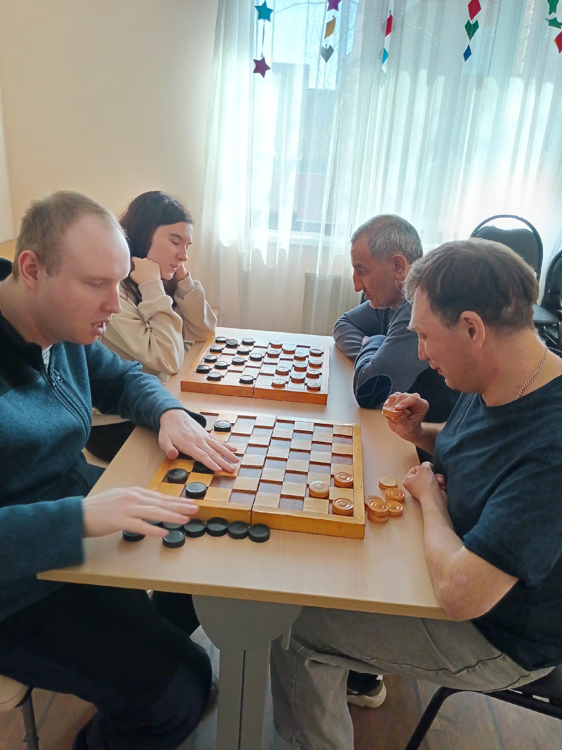 Четыре человека играют в шашки за двумя столами
