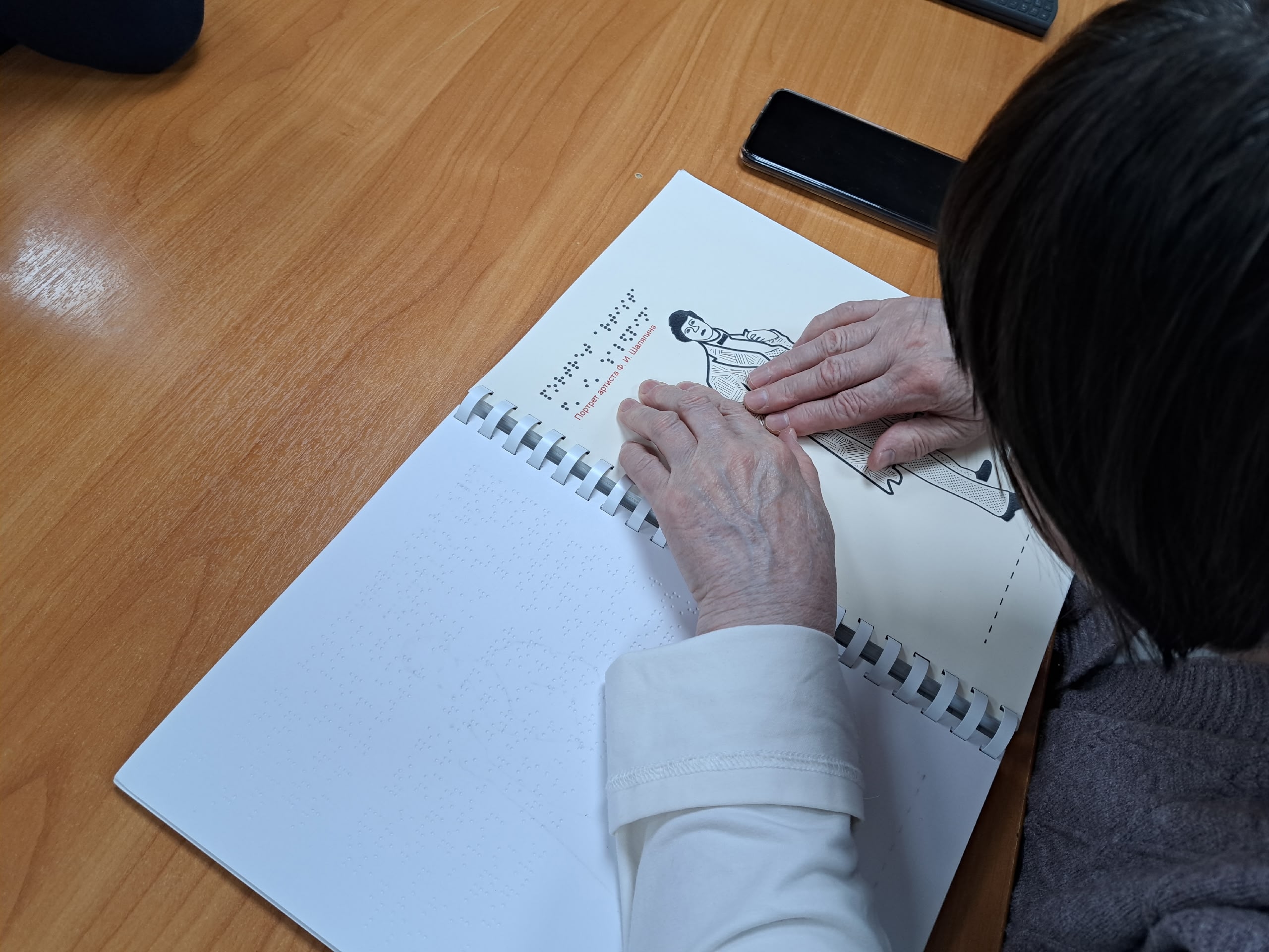 Руки человека касаются тактильного рисунка в книге.