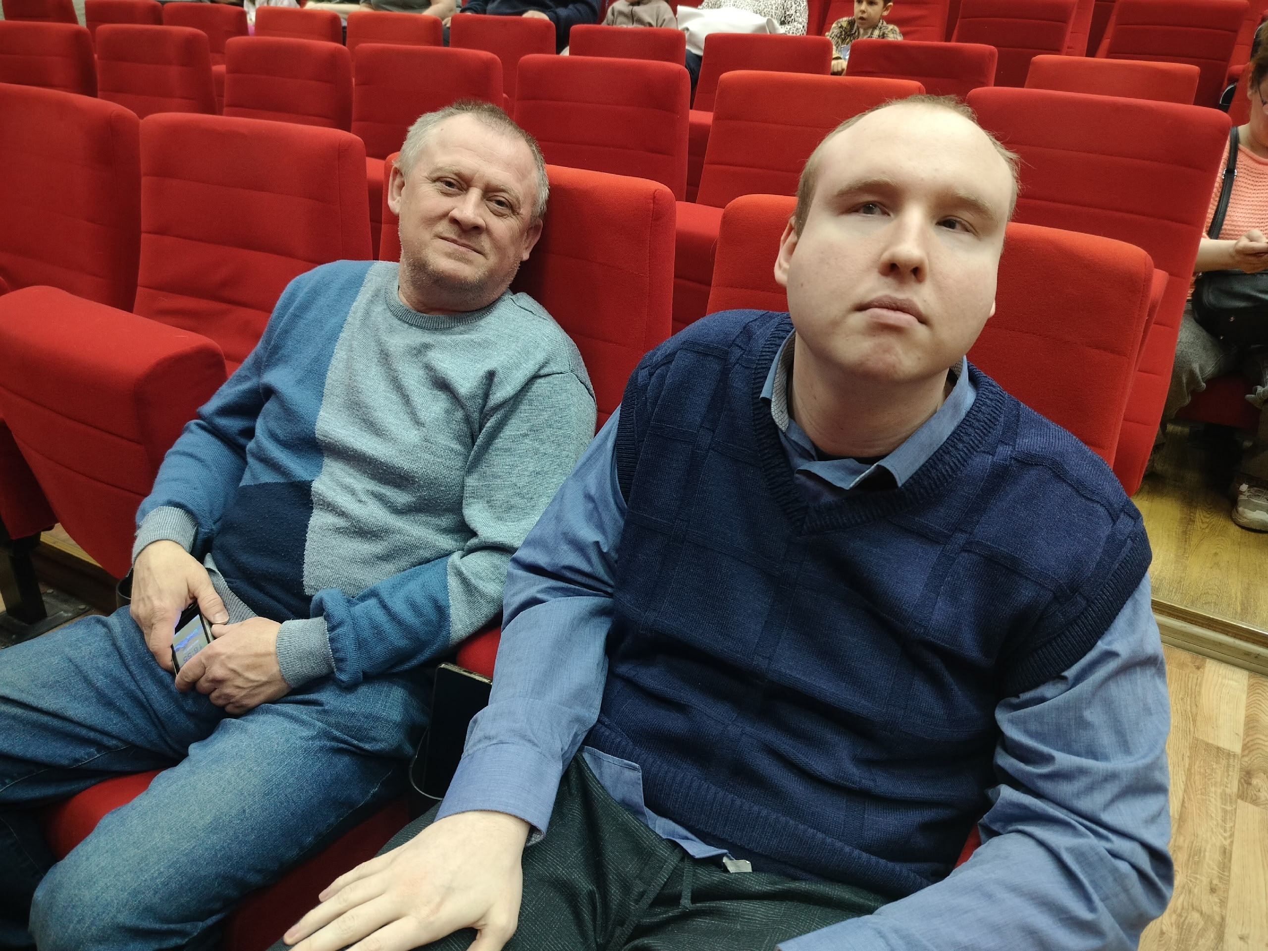 Два мужчины сидят в зале перед сценой