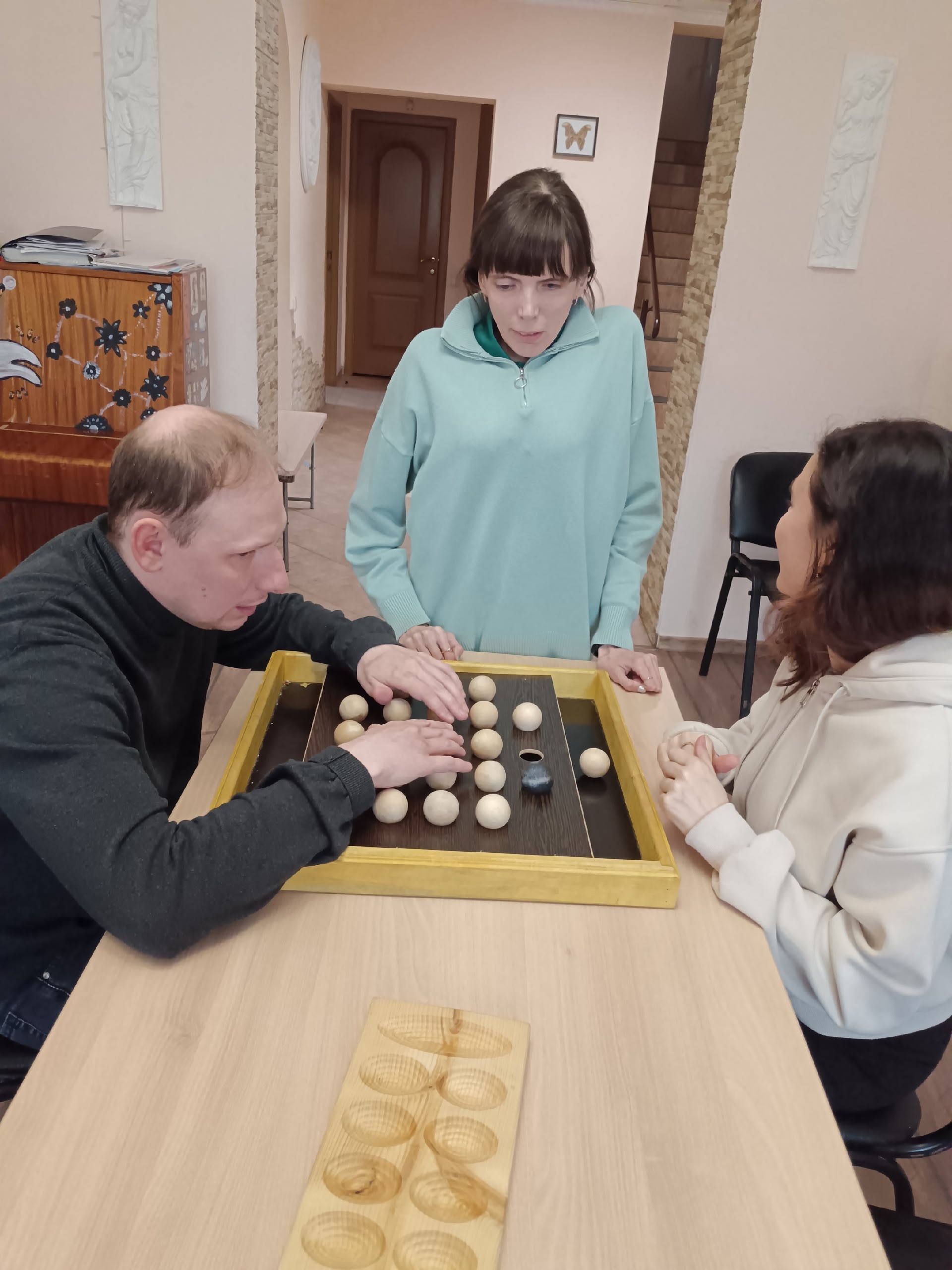 Мужчина играет в настольную игру, две женщины наблюдают