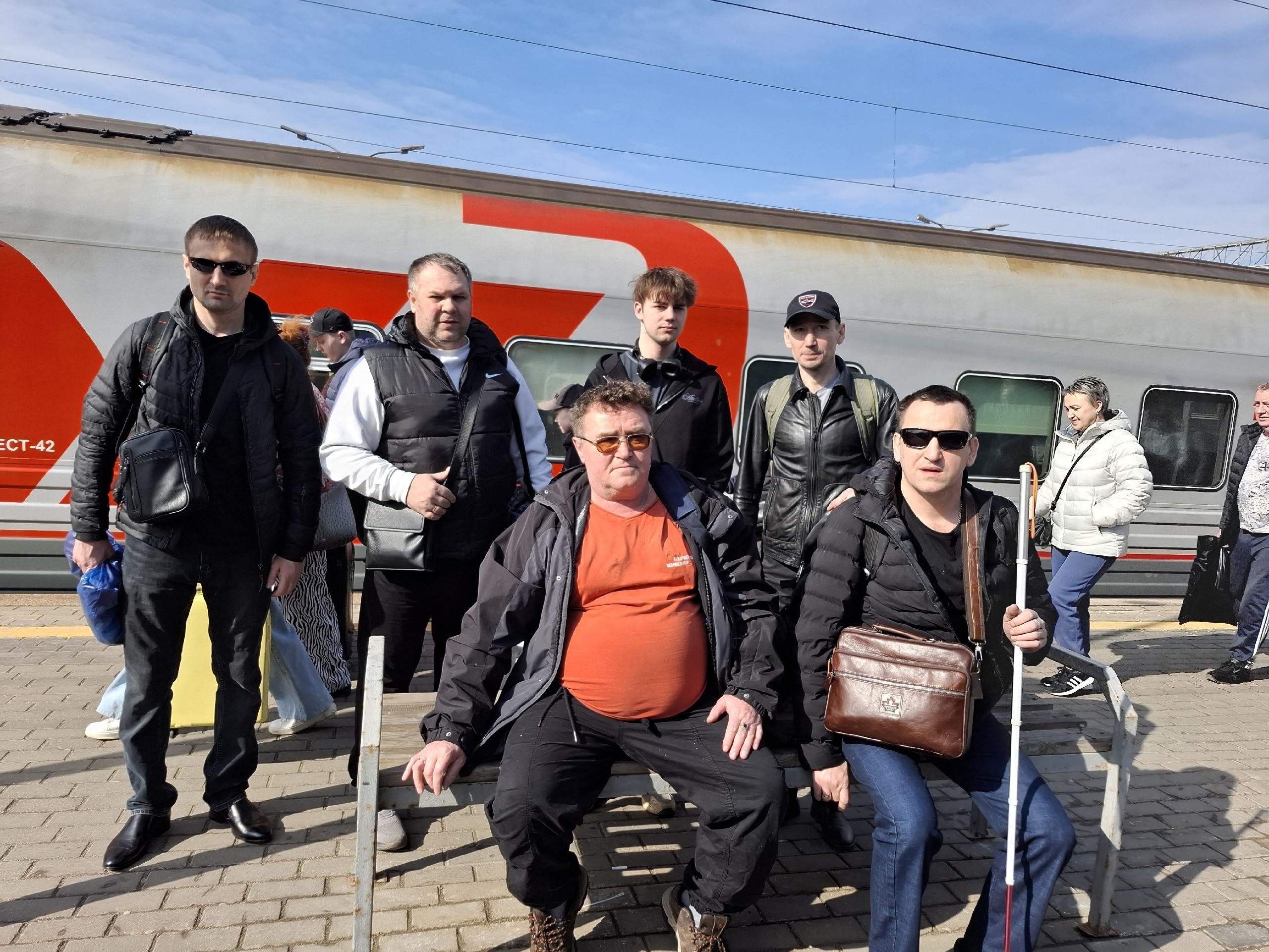 Группа мужчин на железнодорожной платформе, один из них с белой тростью