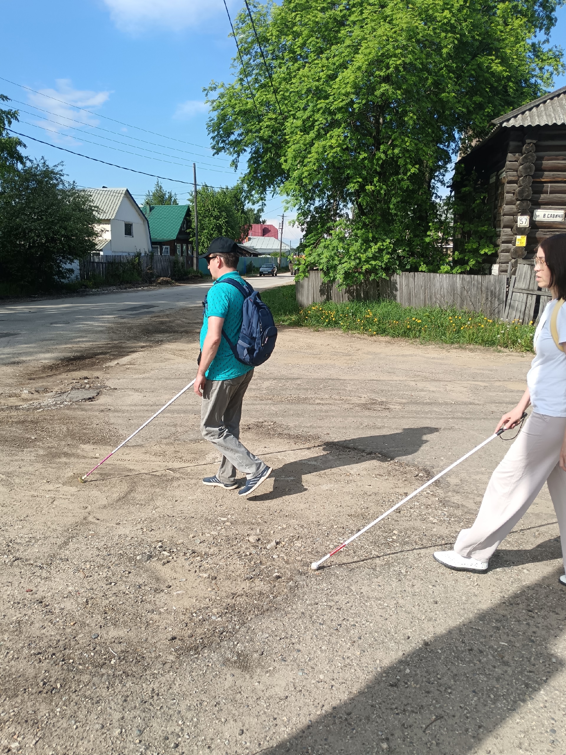 Двое людей с тростями идут по грунтовой дороге в частном секторе