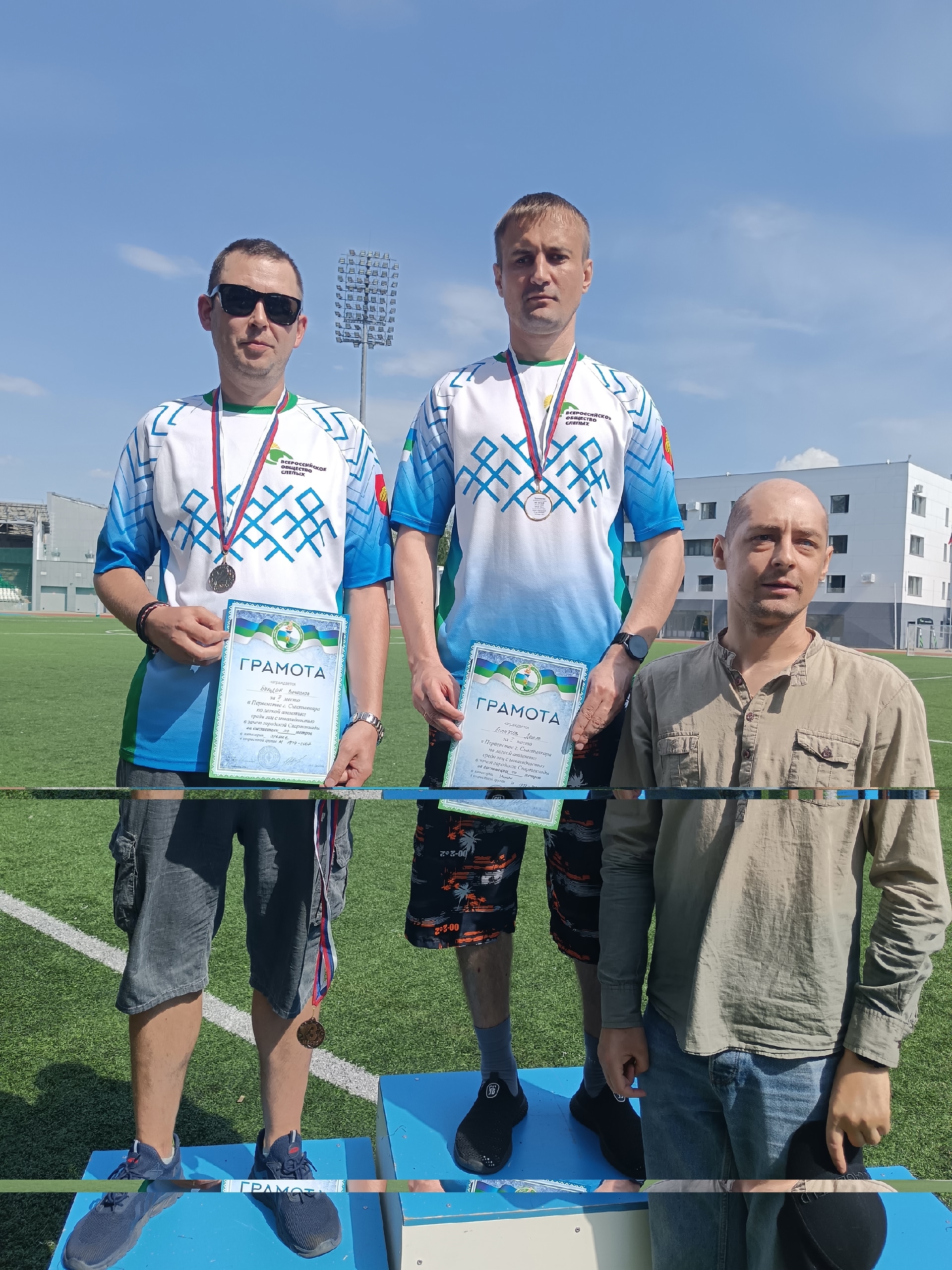 Двое мужчин с медалями и грамотами стоят на пьедестале почета