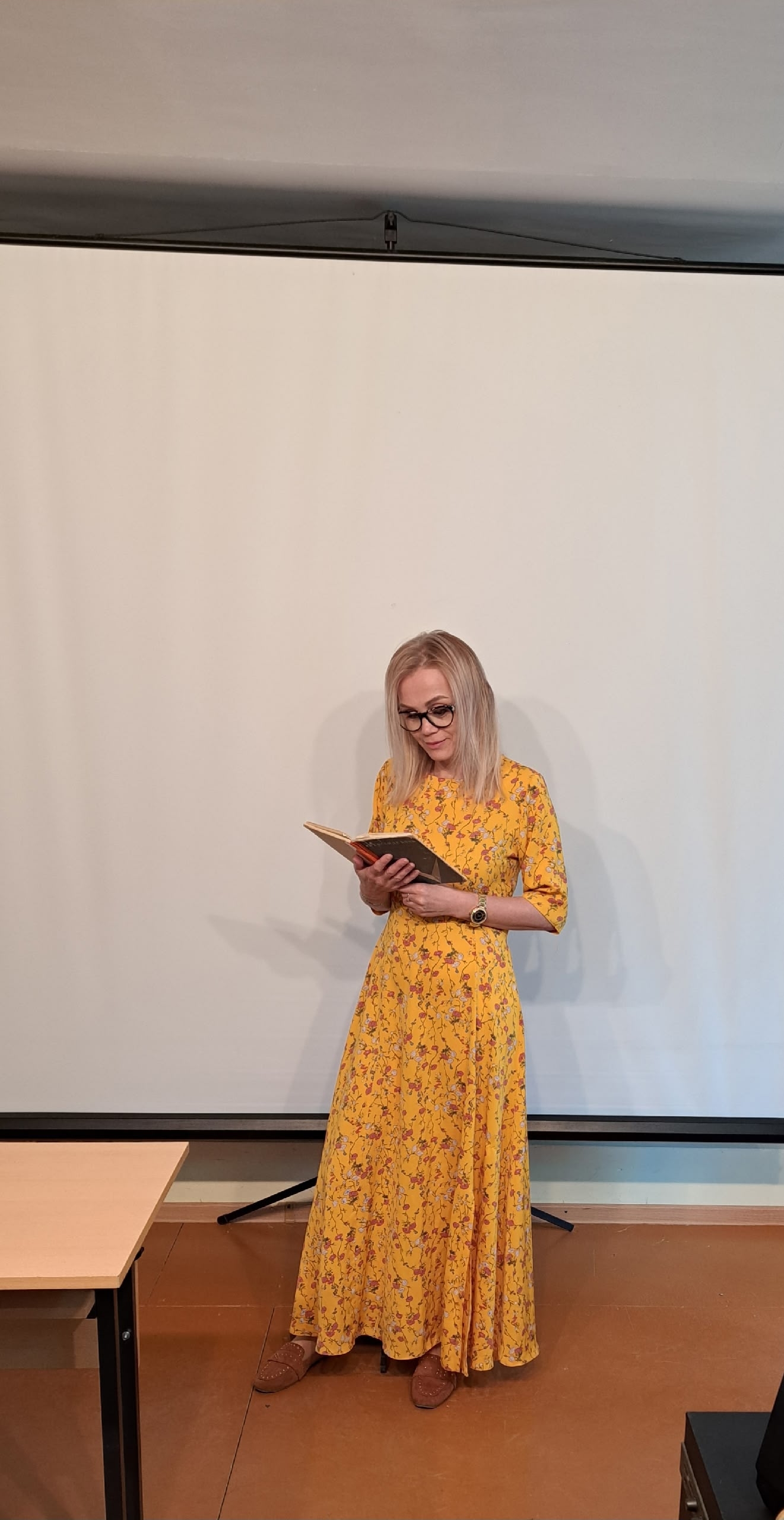 Женщина в желтом платье читает книгу на фоне белого экрана