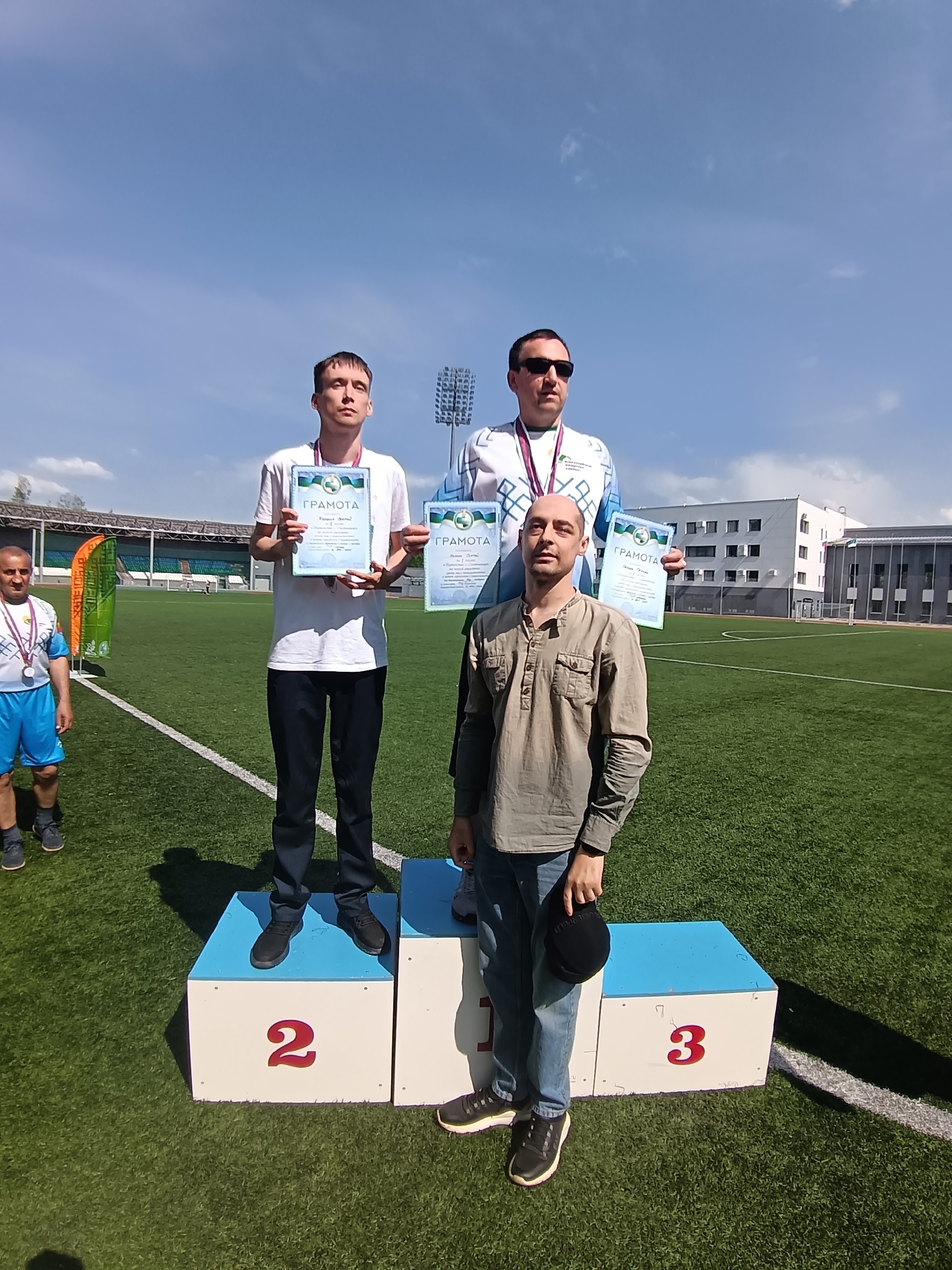 Двое спортсменов с грамотами стоят на пьедестале почета