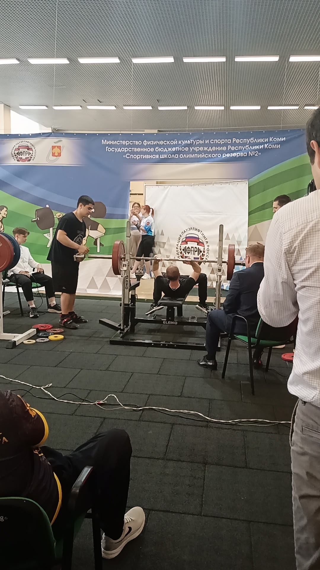 Атлет в черной форме выполняет жим штанги на соревнованиях