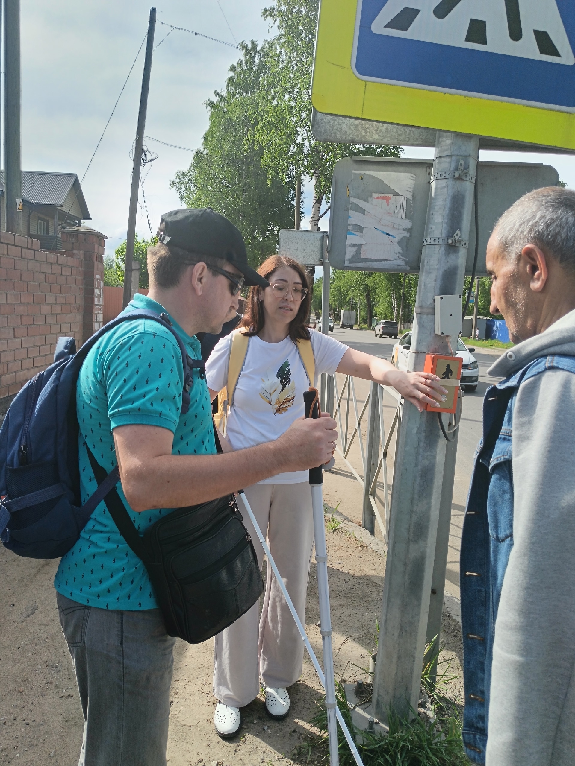Женщина нажимает кнопку светофора для пешеходов рядом с мужчиной