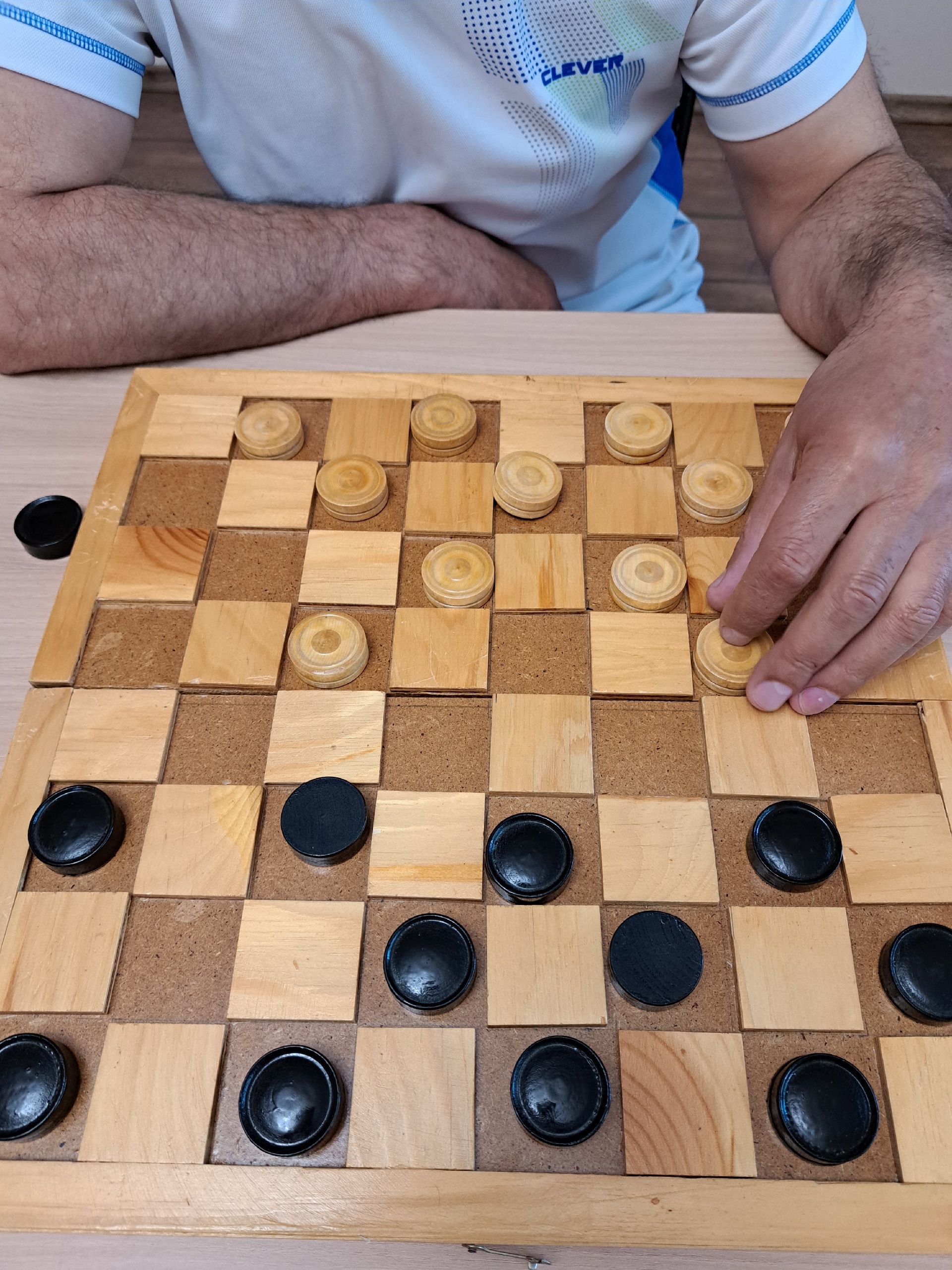 Рука игрока передвигает шашку на деревянной доске