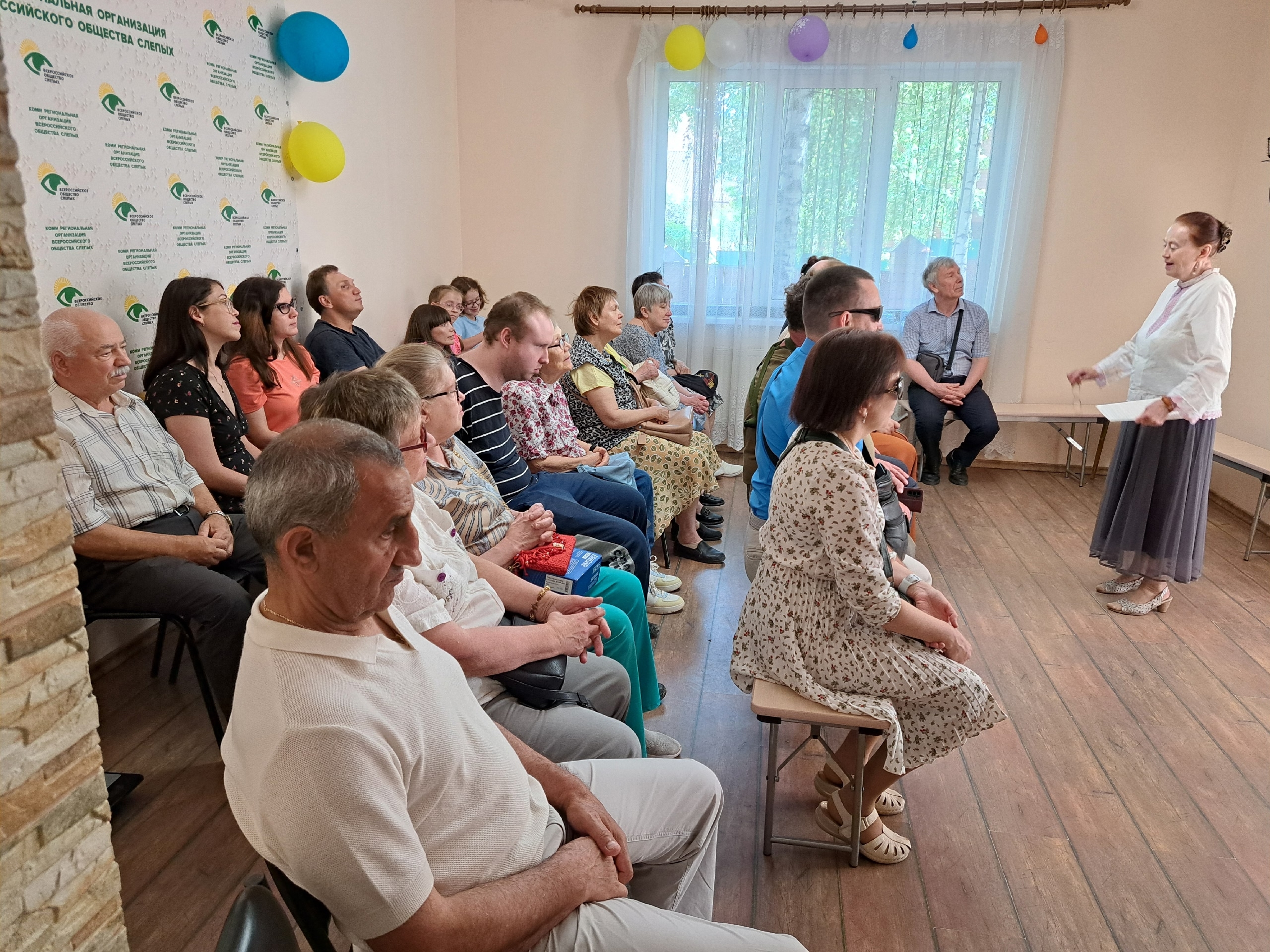 Женщина в белой блузке выступает перед аудиторией в помещении