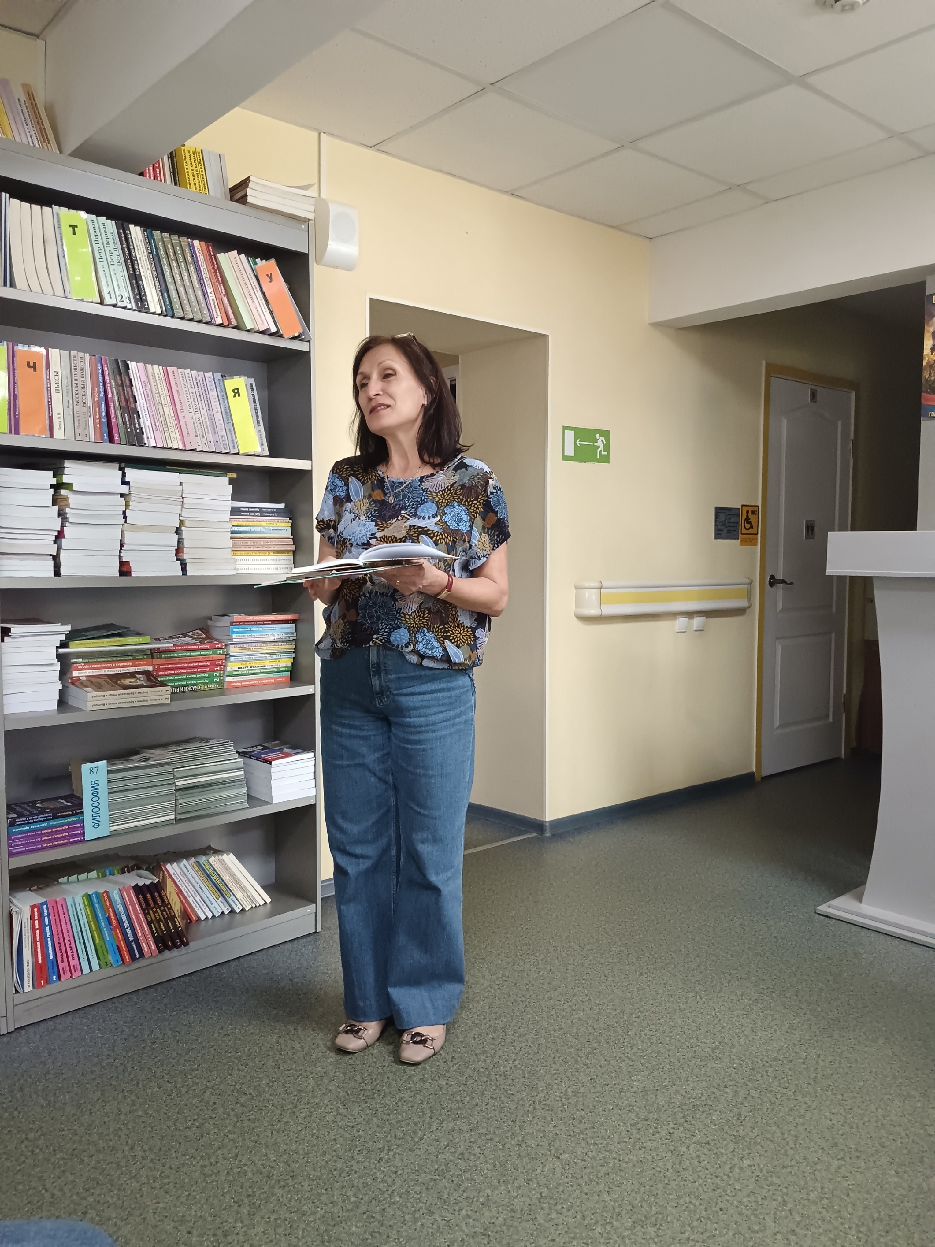 Женщина в блузке с цветочным принтом стоит рядом с книжными полками