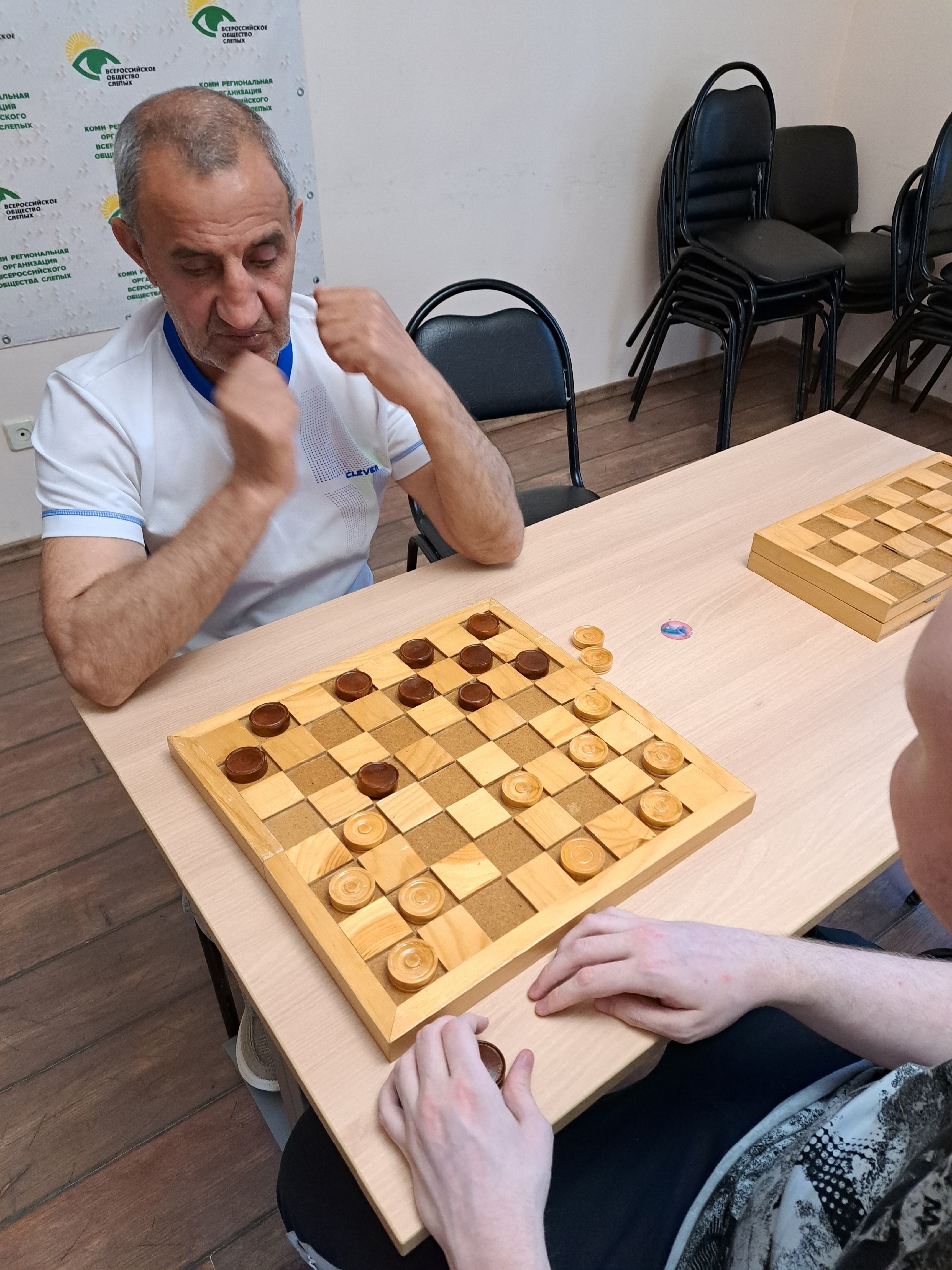 Мужчина в белой футболке обдумывает ход в шашки
