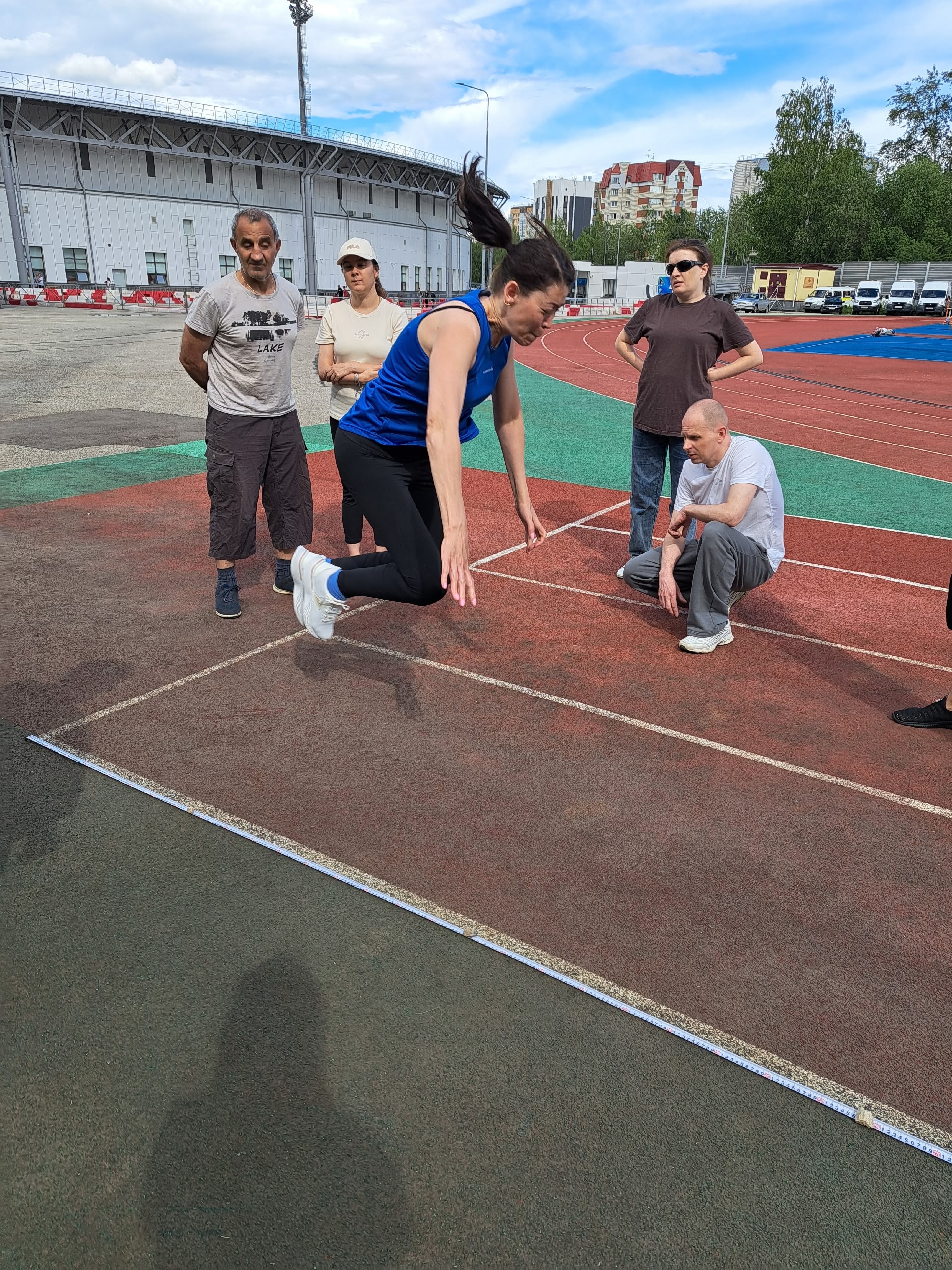 Женщина совершает прыжок в длину под присмотром группы людей