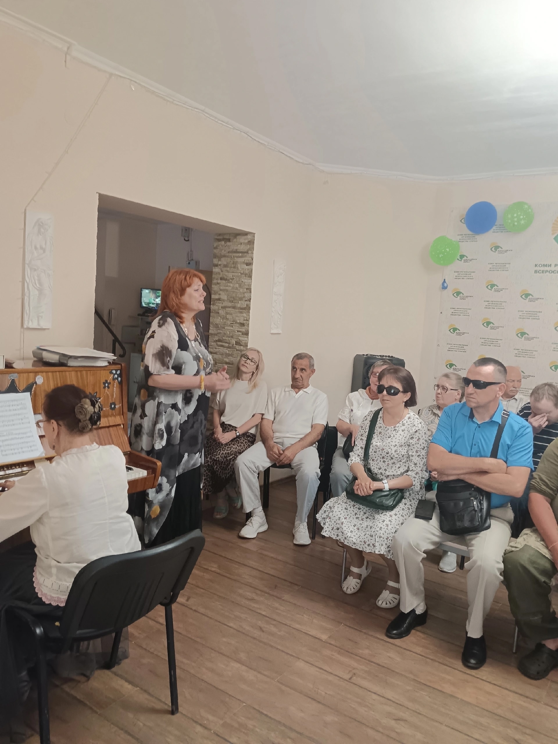 Женщина в платье с цветочным принтом выступает перед зрителями у пианино