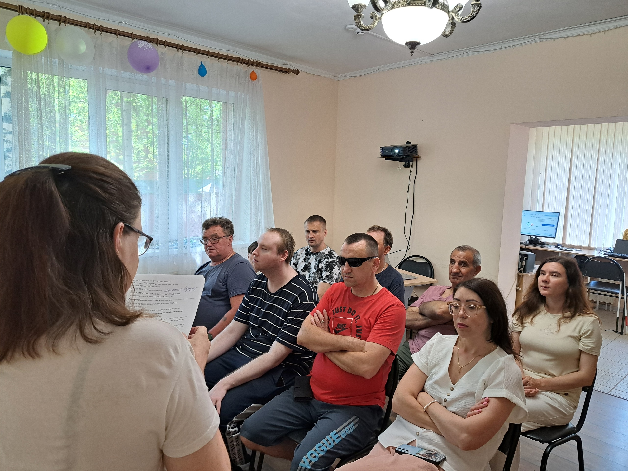 Женщина читает текст перед группой внимательно слушающих людей в помещении
