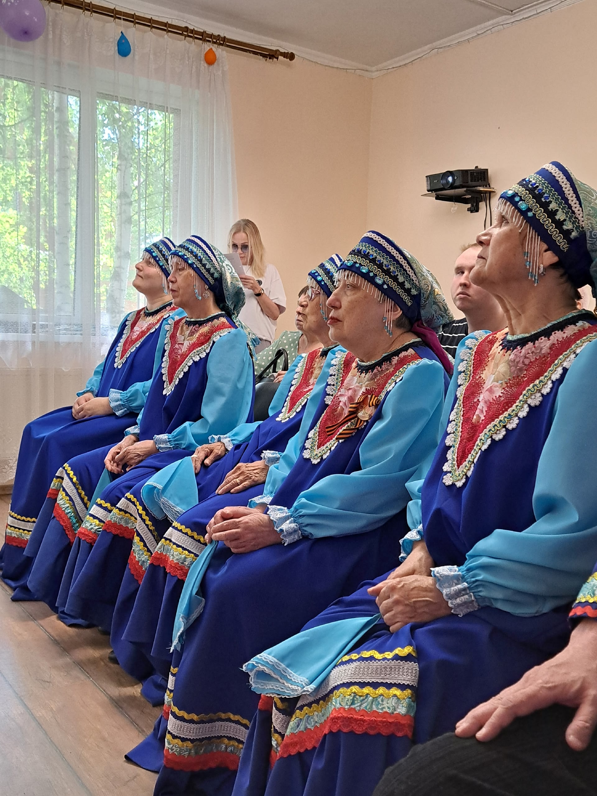 Женщины в народных костюмах сидят в зале