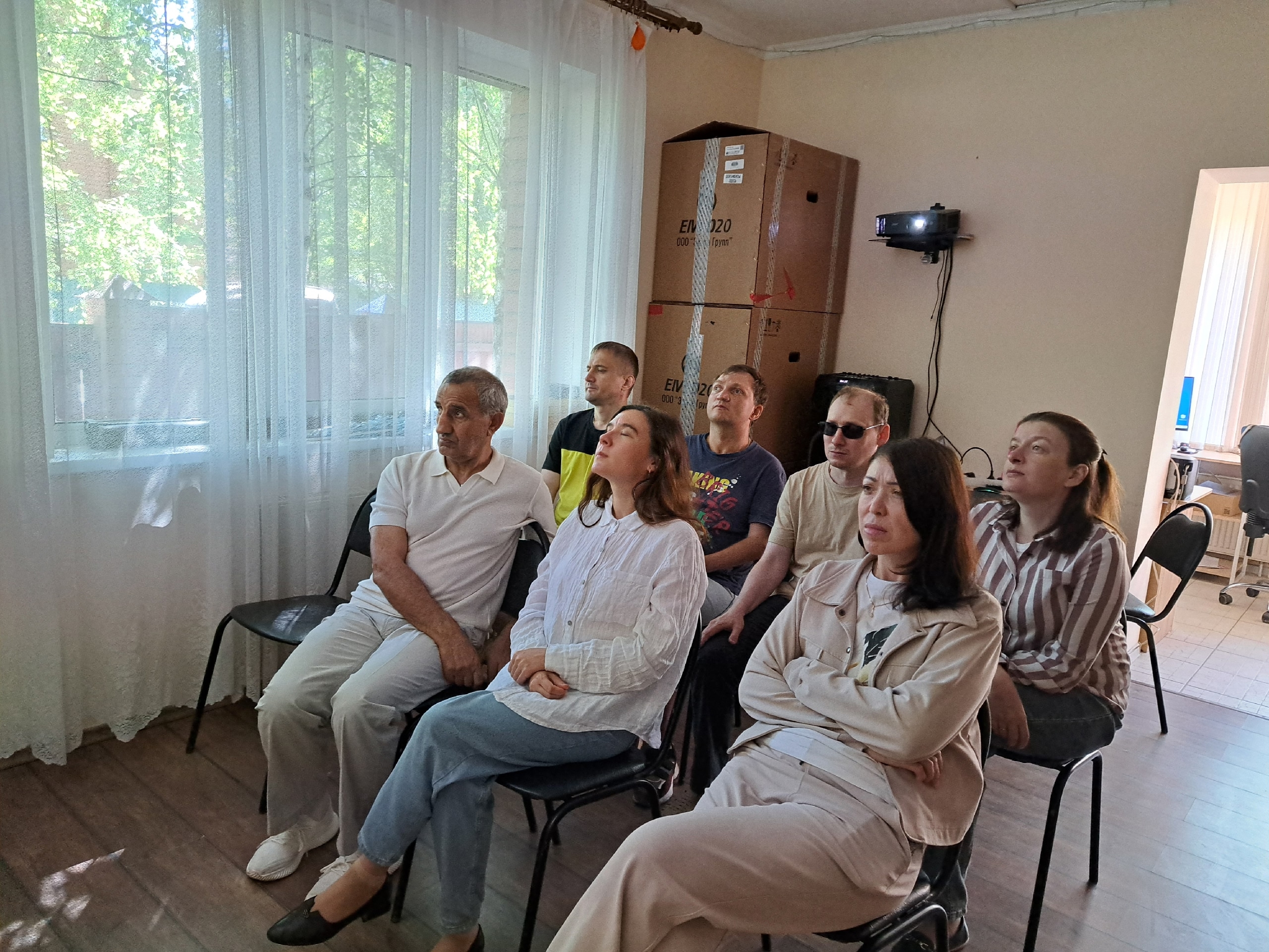 Люди сидят на стульях в помещении и внимательно смотрят в сторону