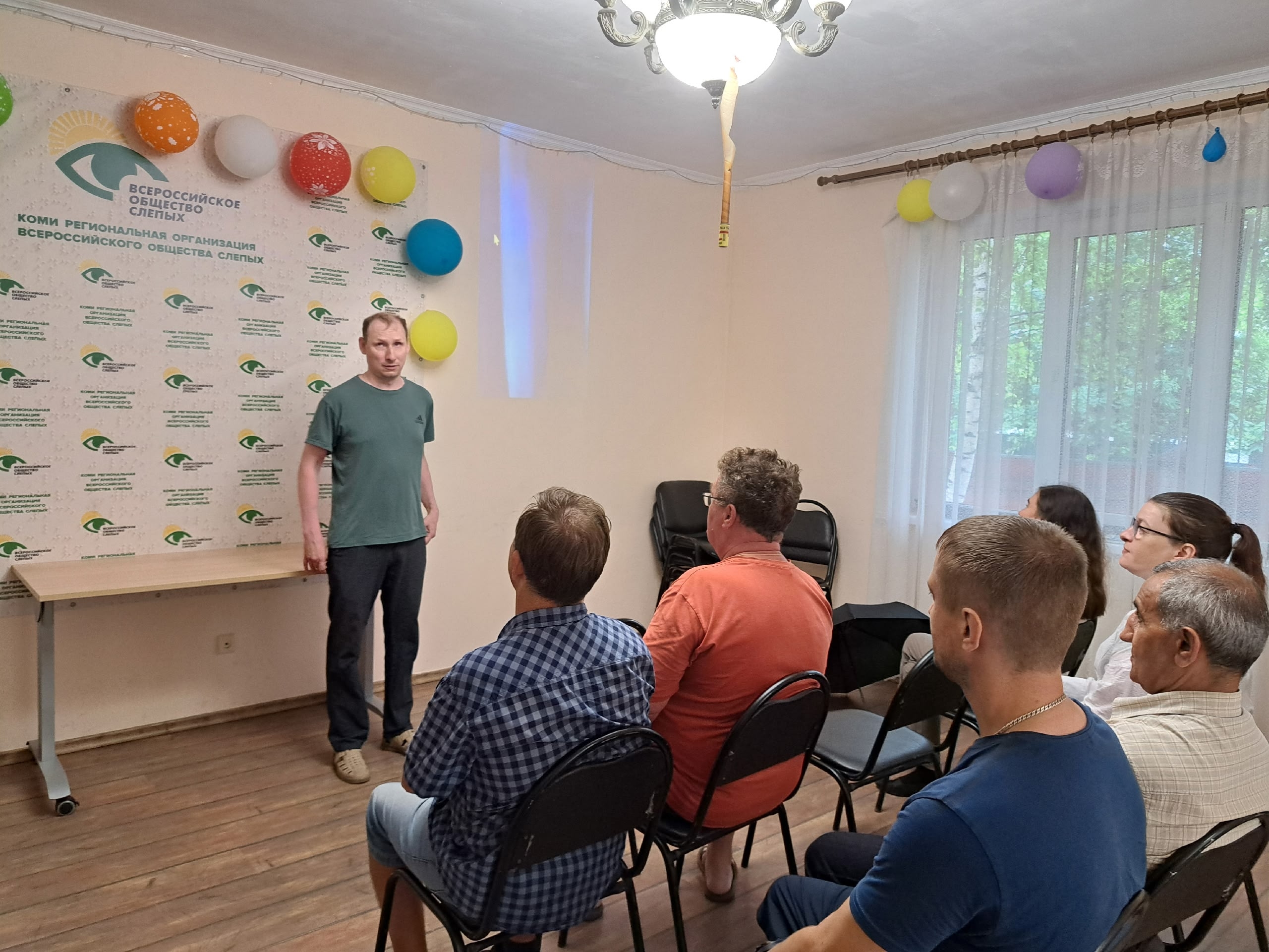 Мужчина выступает перед аудиторией в помещении с воздушными шарами