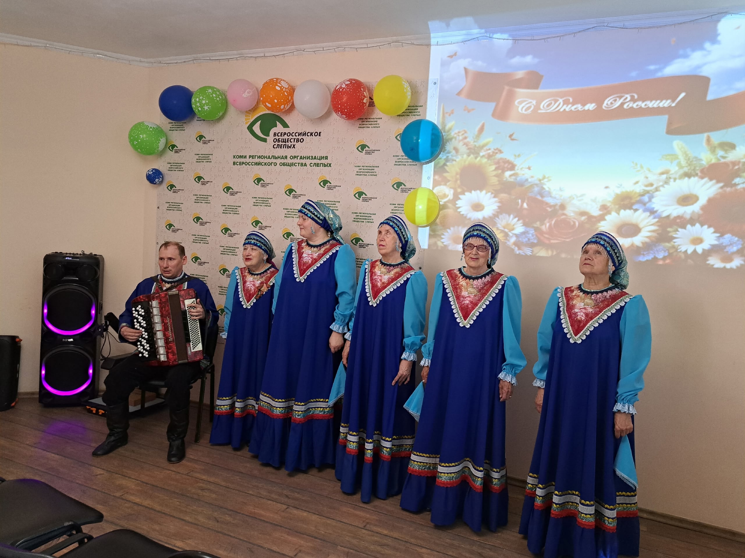 Мужчина с гармонью и хор в народных костюмах на сцене