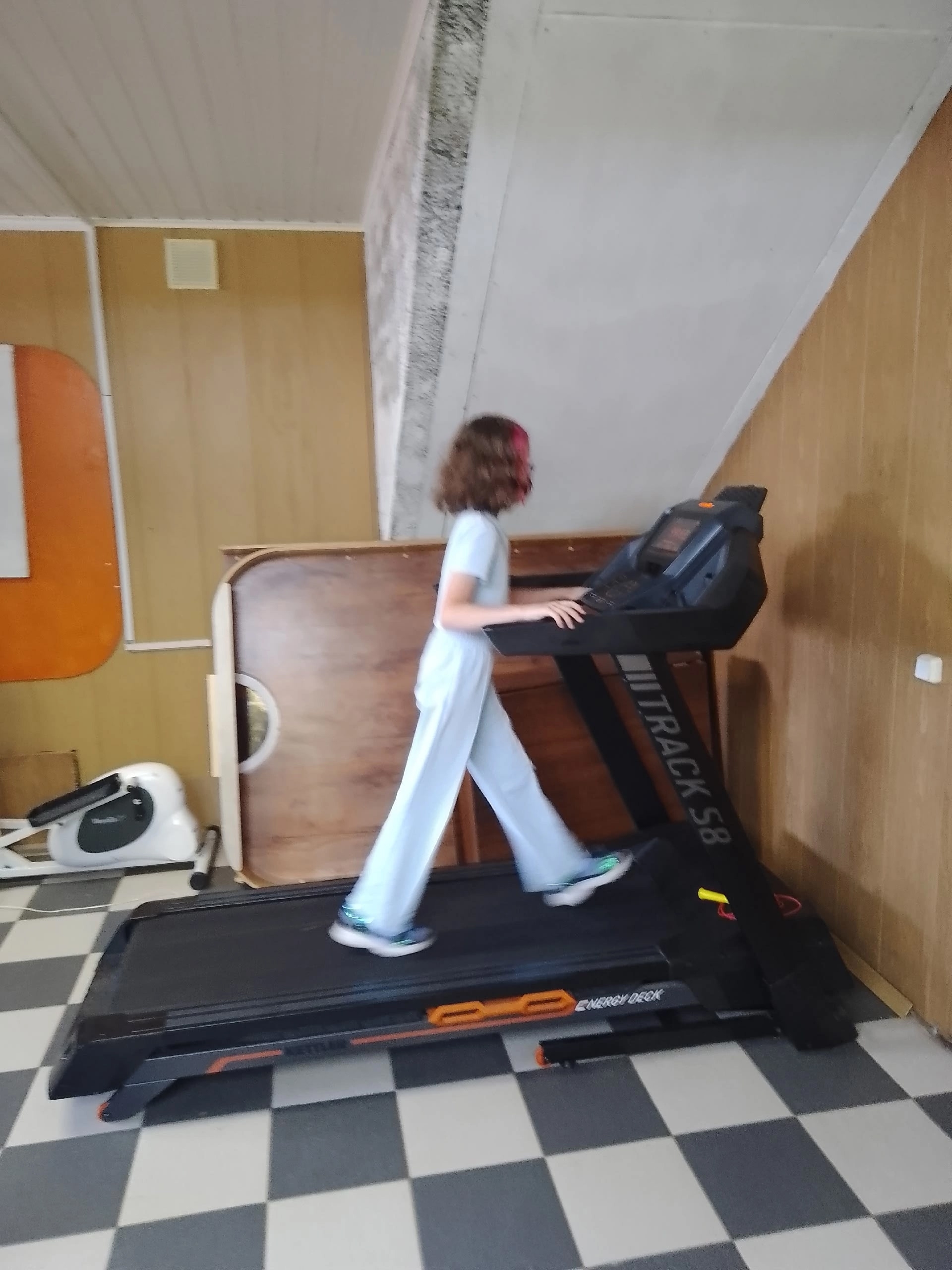 Девушка в светлом костюме идет по беговой дорожке