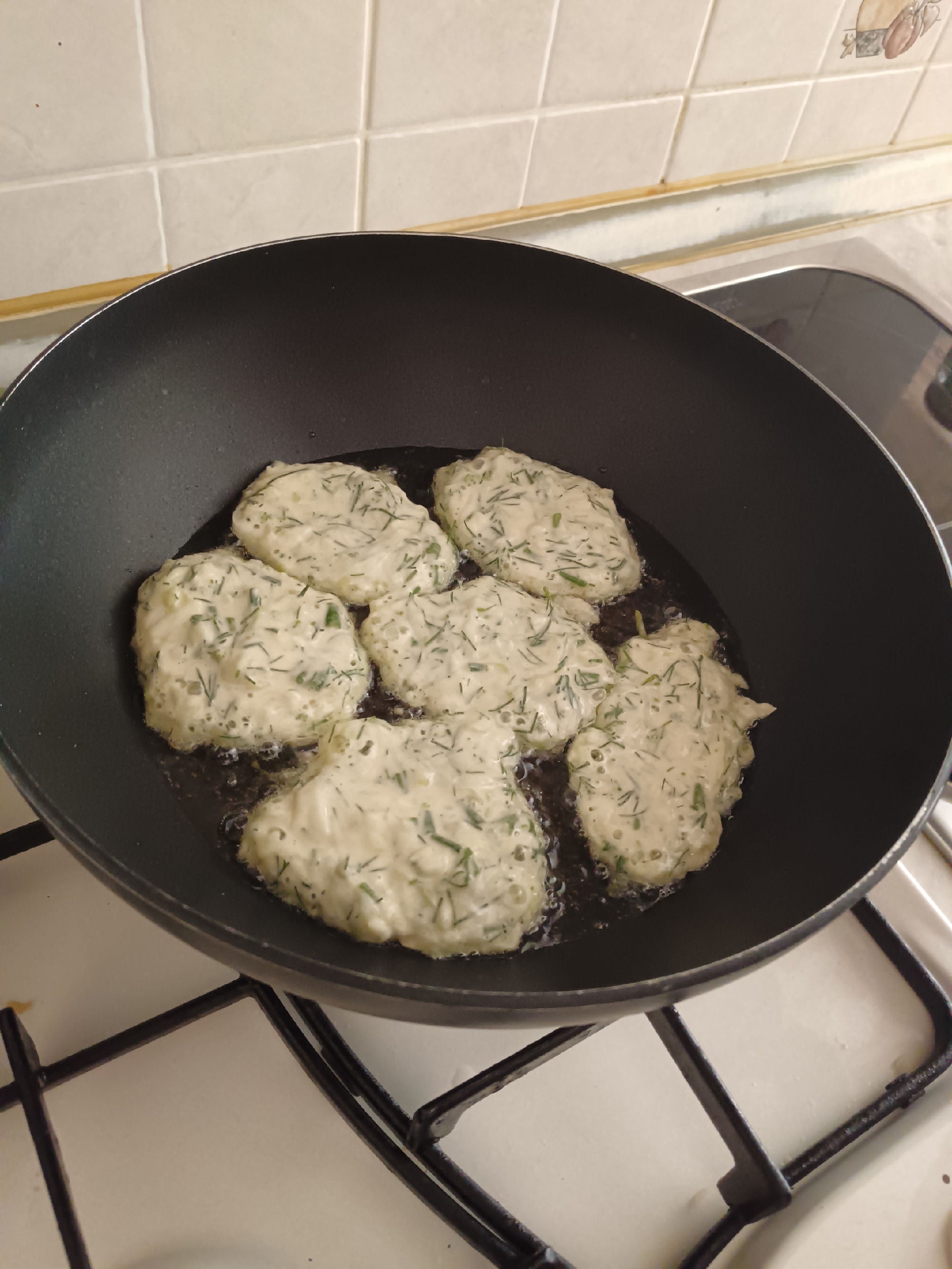 Кабачковые оладьи с зеленью жарятся на сковороде с маслом