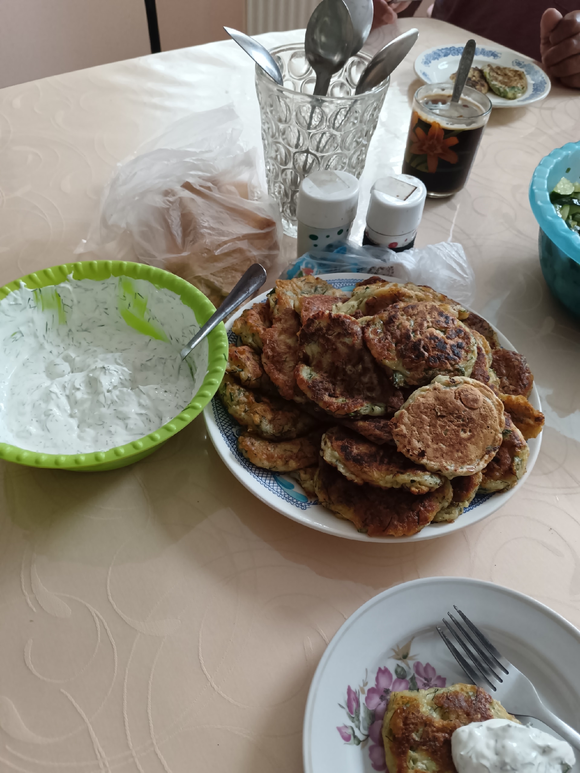 Готовые кабачковые оладьи на тарелке и белый соус в зеленой миске на обеденном столе