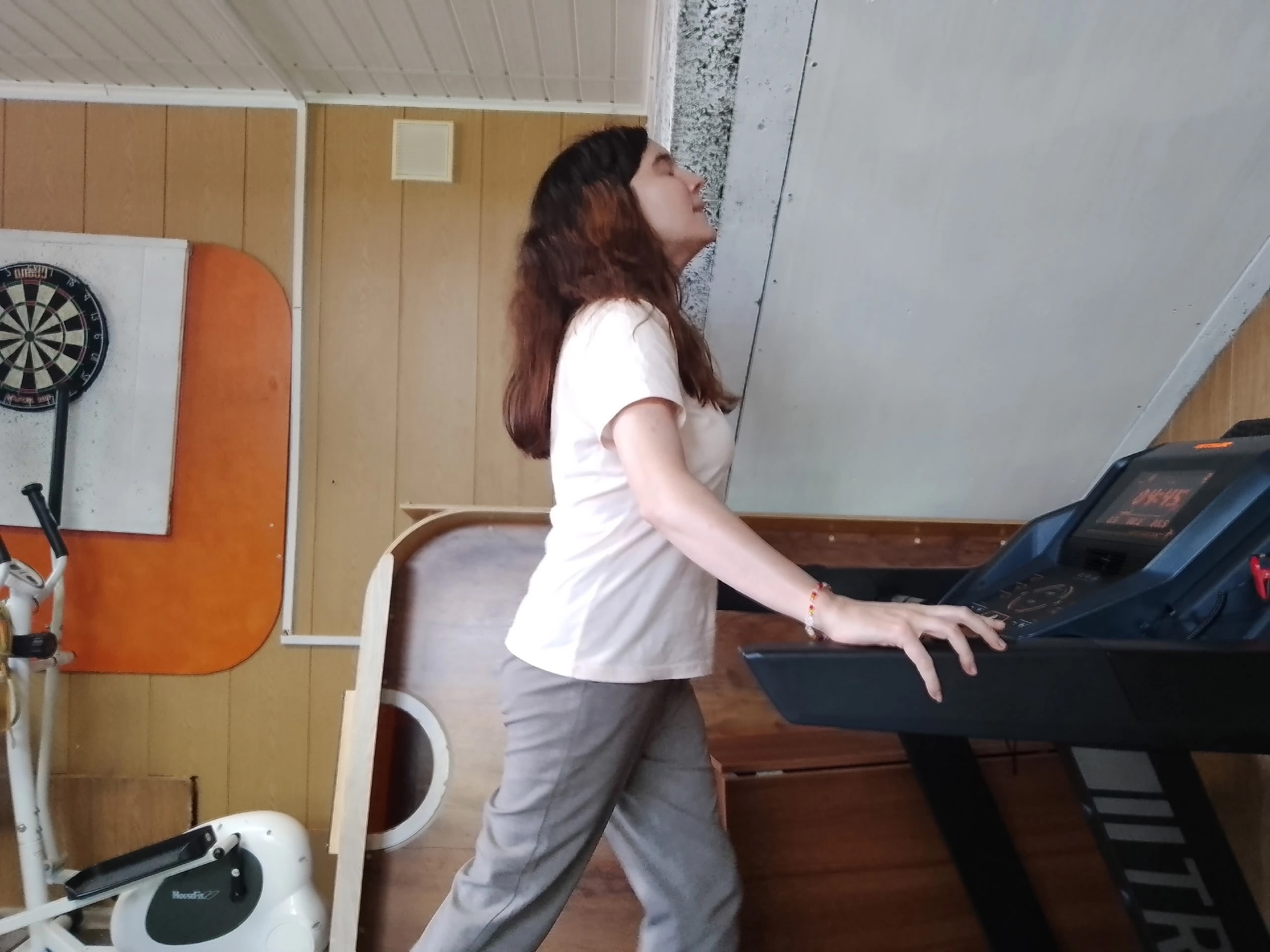 Девушка в белой футболке тренируется на беговой дорожке