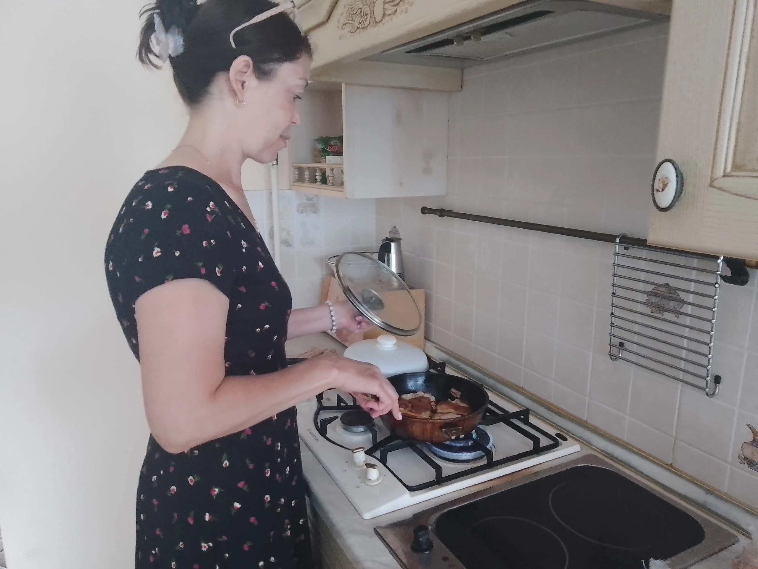 Женщина обжаривает мясо на сковороде, приподнимая стеклянную крышку
