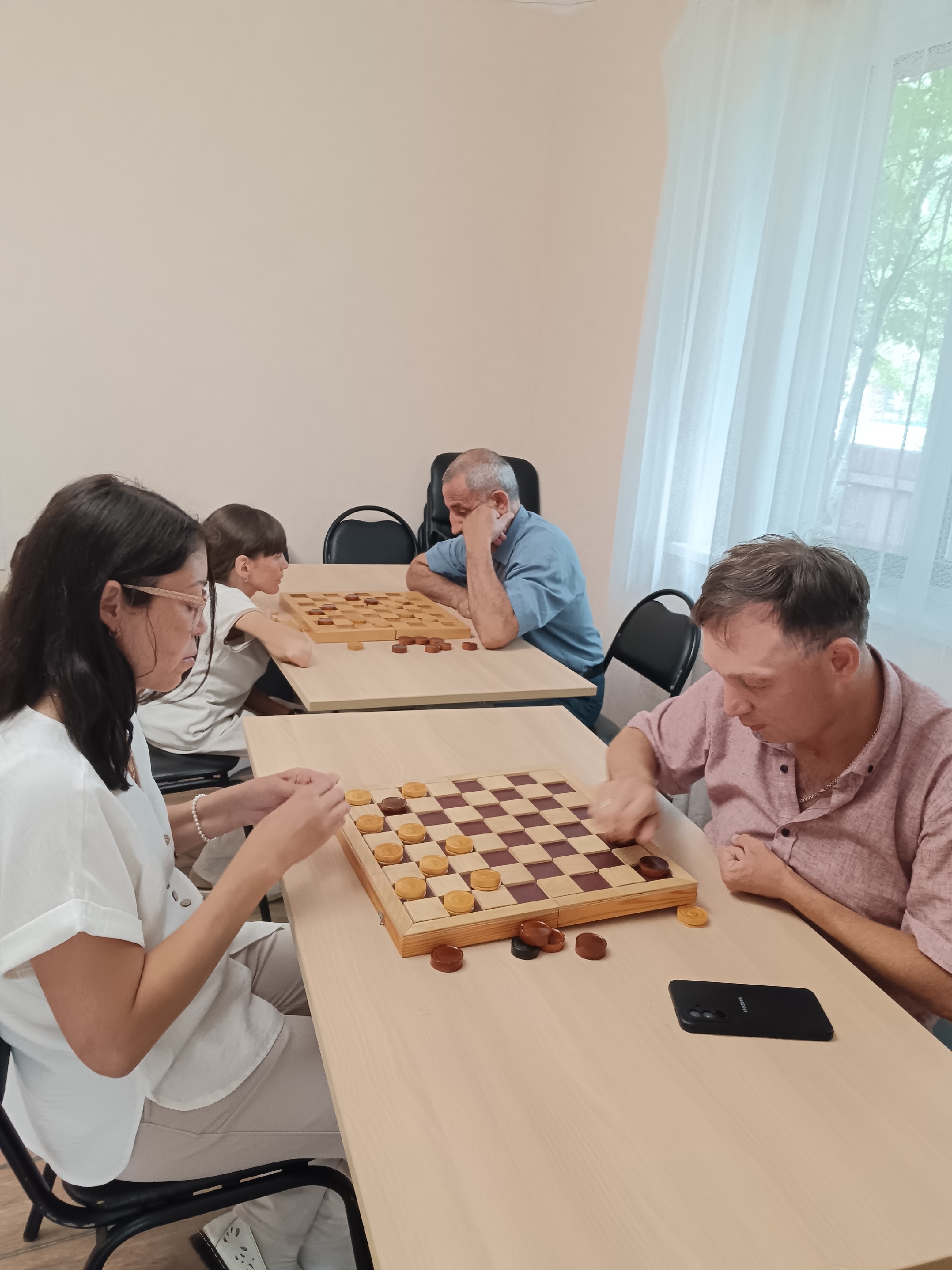 Мужчина и женщина играют в шашки за столом, на переднем плане деревянная доска с фишками