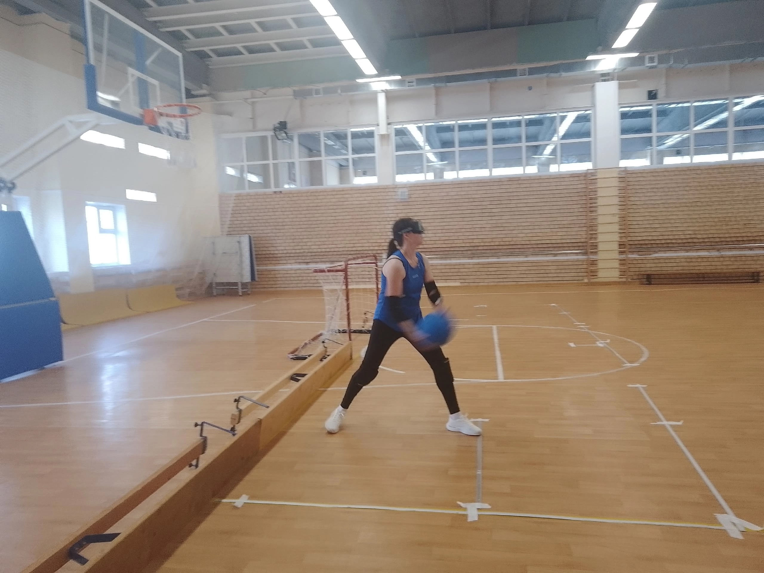 Спортсменка в светонепроницаемых очках держит синий мяч в спортивном зале