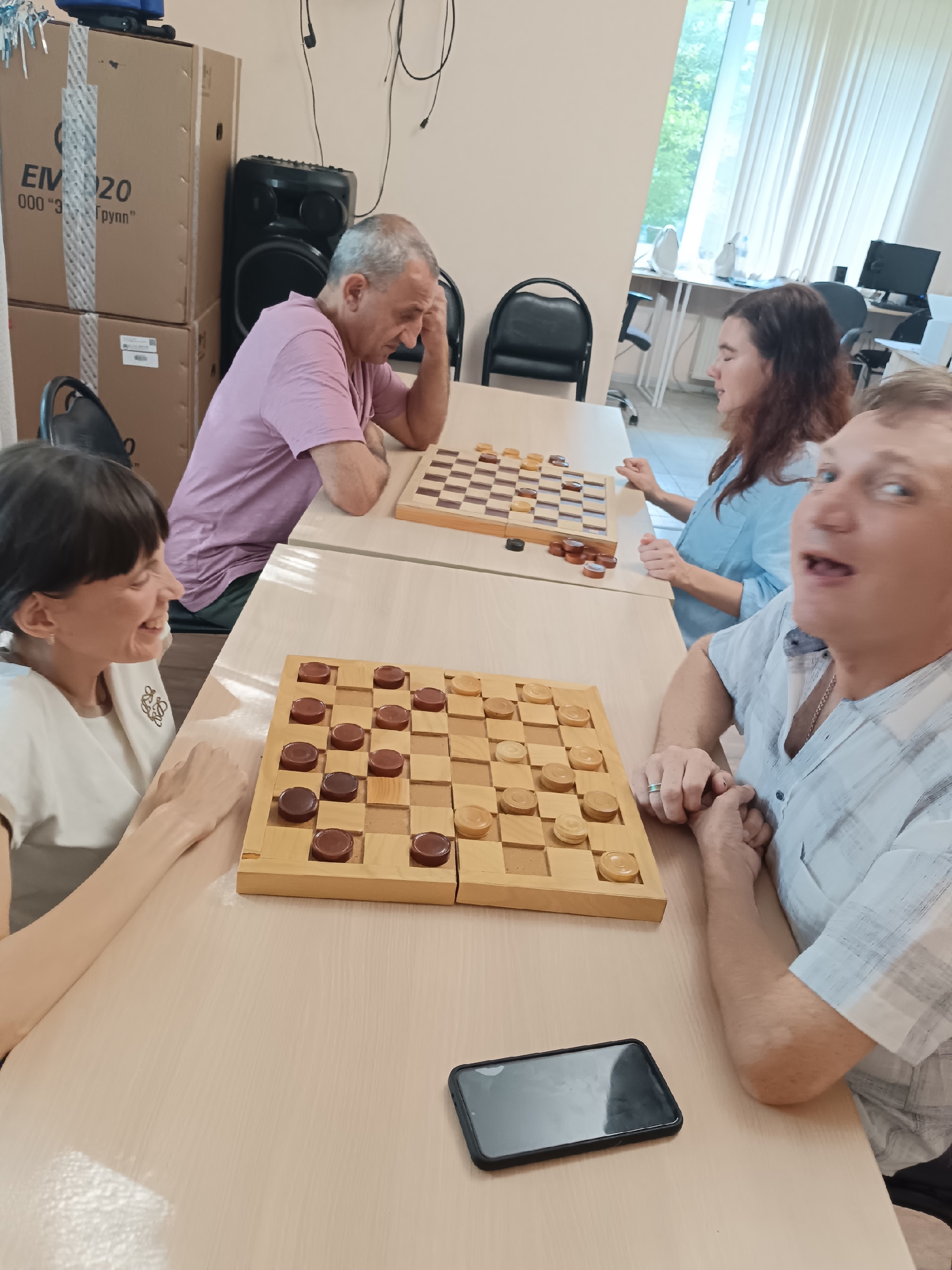 Две пары игроков сидят за длинным столом и играют в шашки
