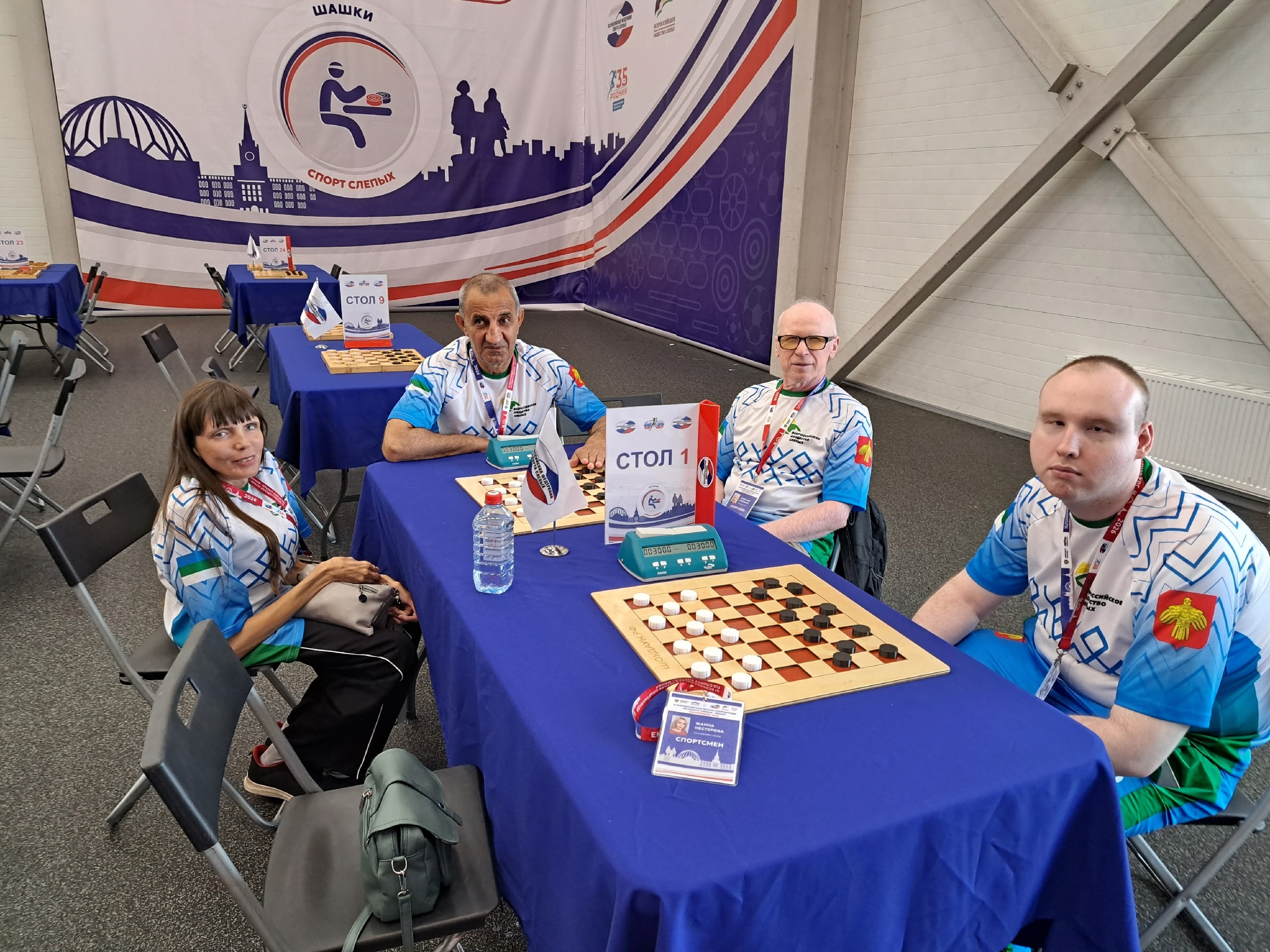 Четыре спортсмена в игровой форме сидят за столом с шашечной доской