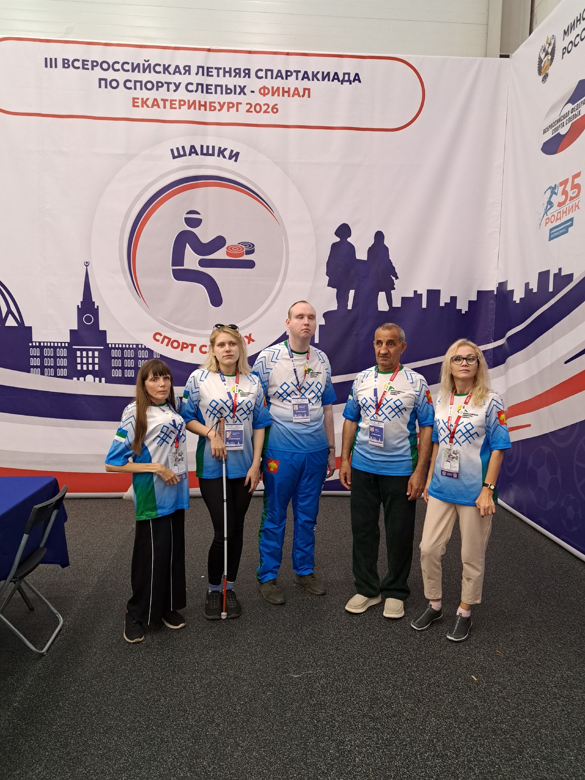 Группа спортсменов в спортивной форме позирует на фоне баннера соревнований