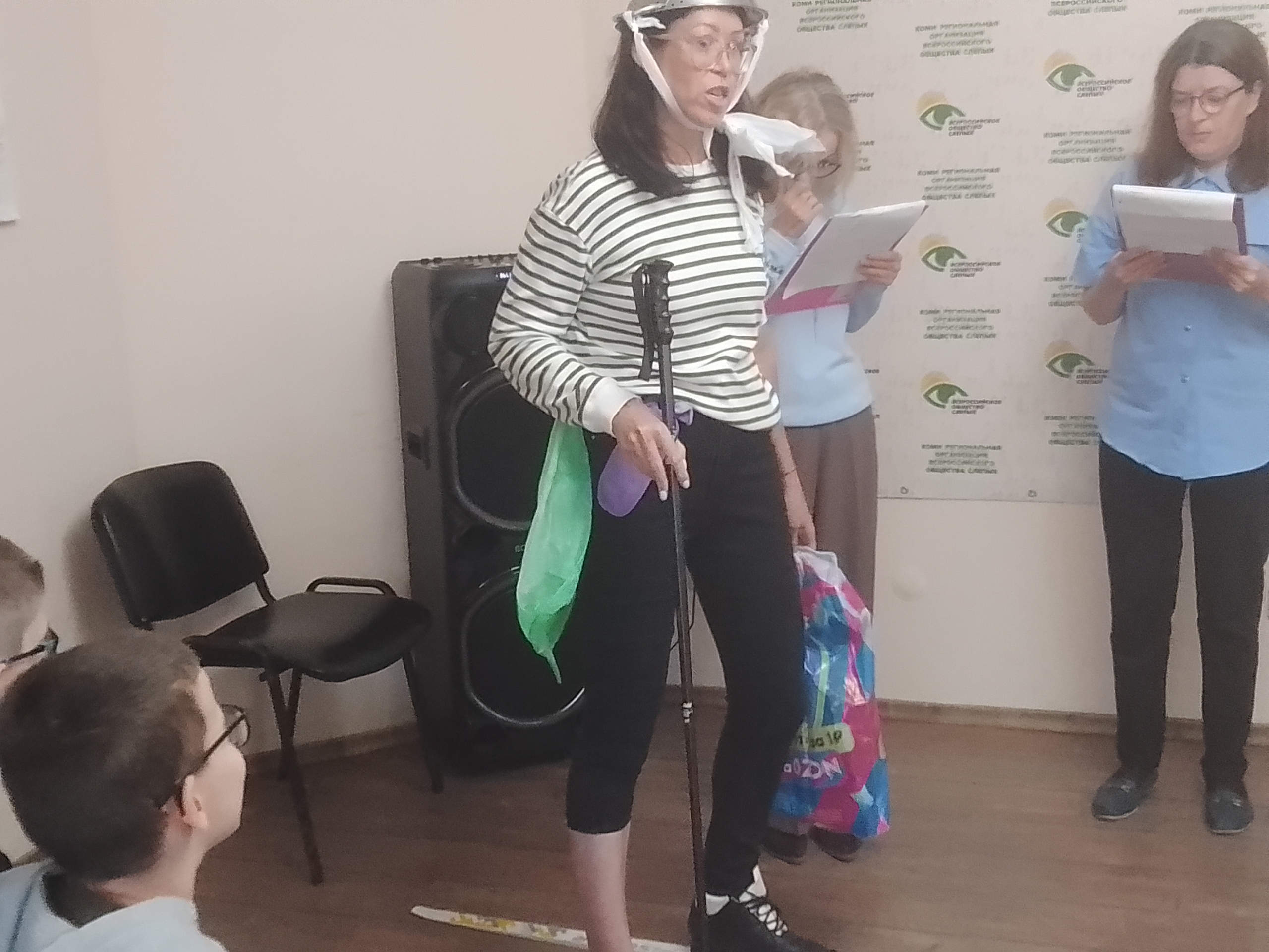 Женщина в полосатой кофте и шуточном шлеме выступает перед детьми
