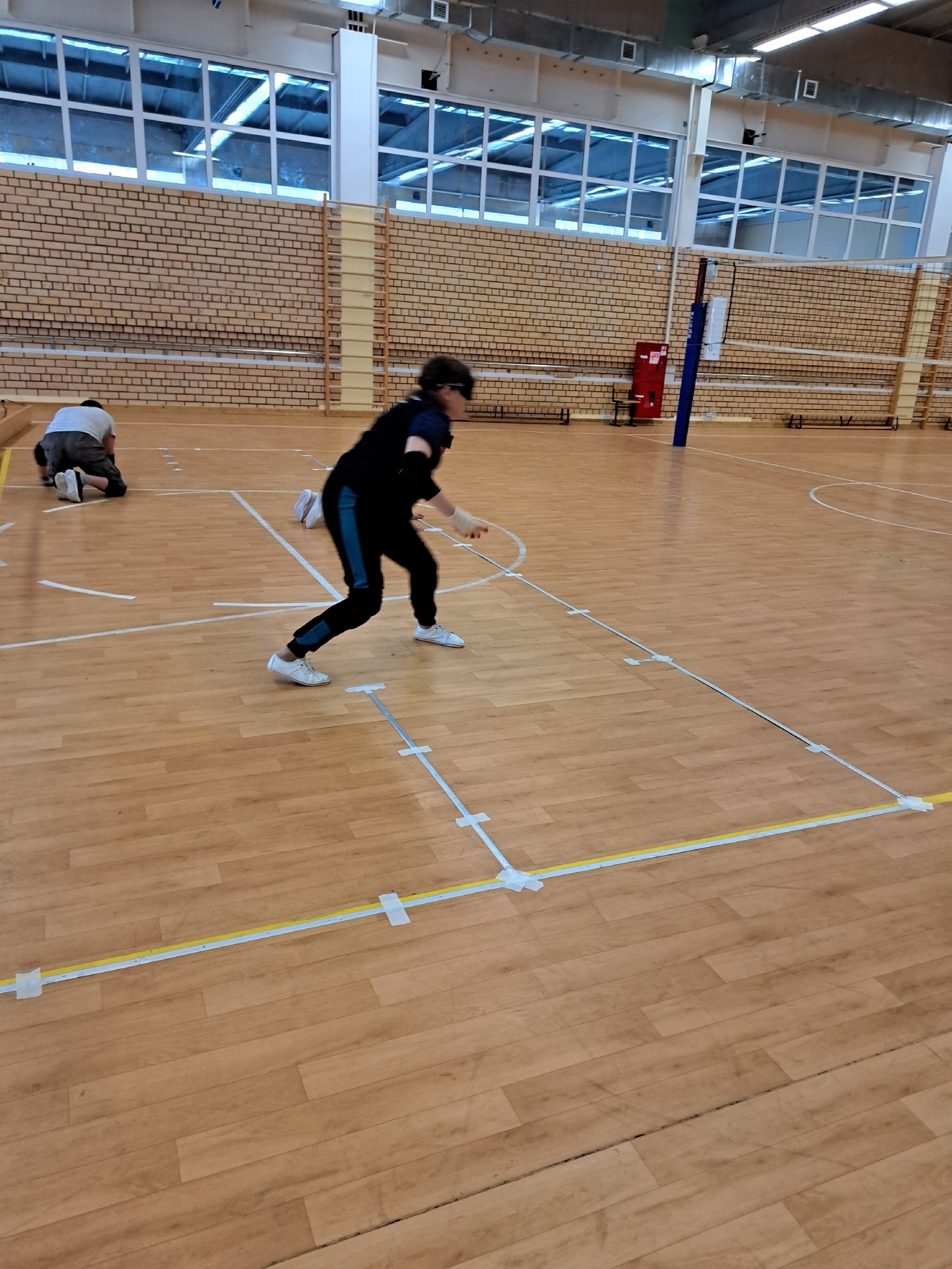 Спортсмен в маске для голбола тренируется на деревянном полу в спортивном зале